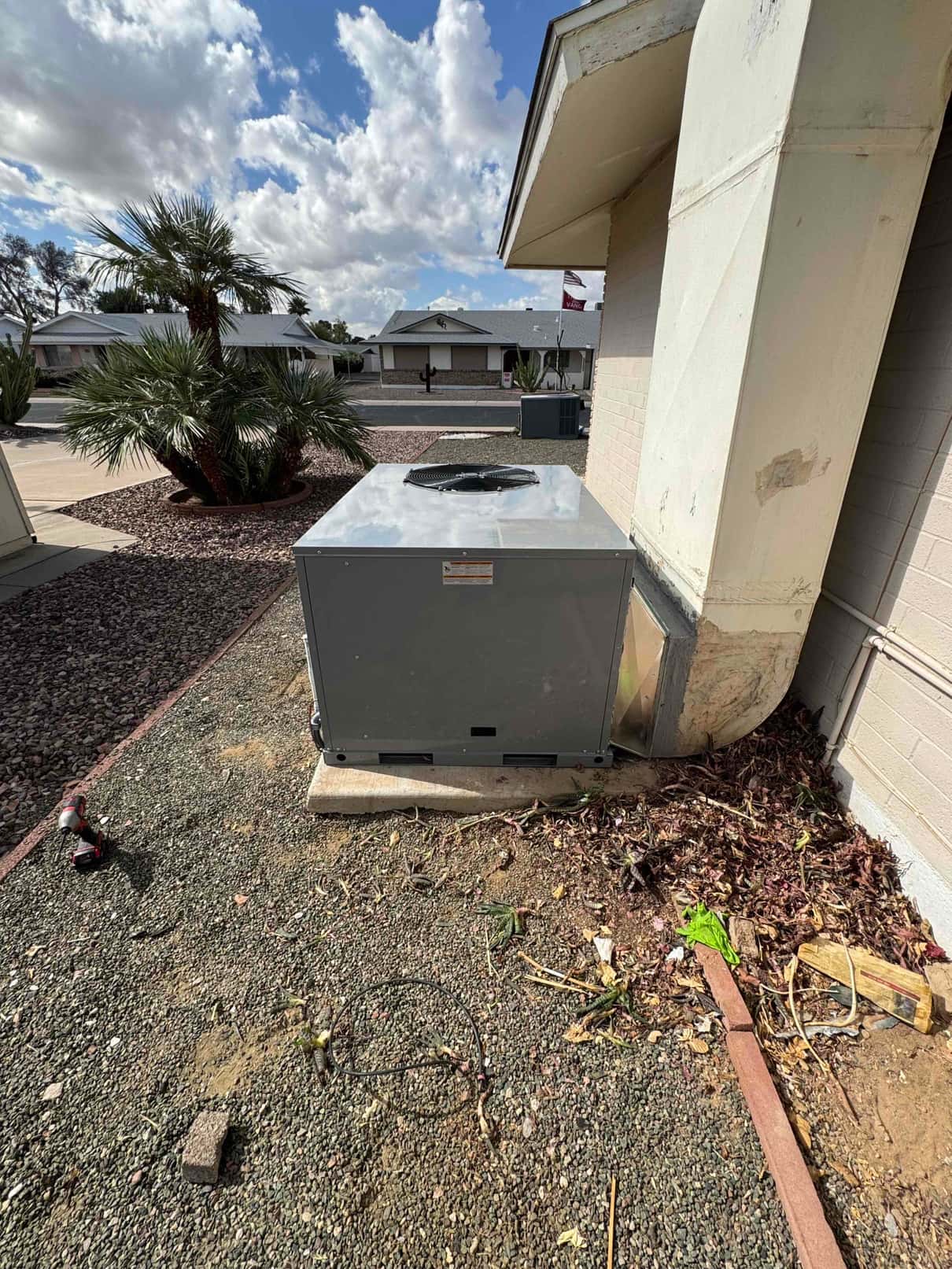 New package HVAC unit set on a level pad with connected duct transition at the exterior wall of the home.