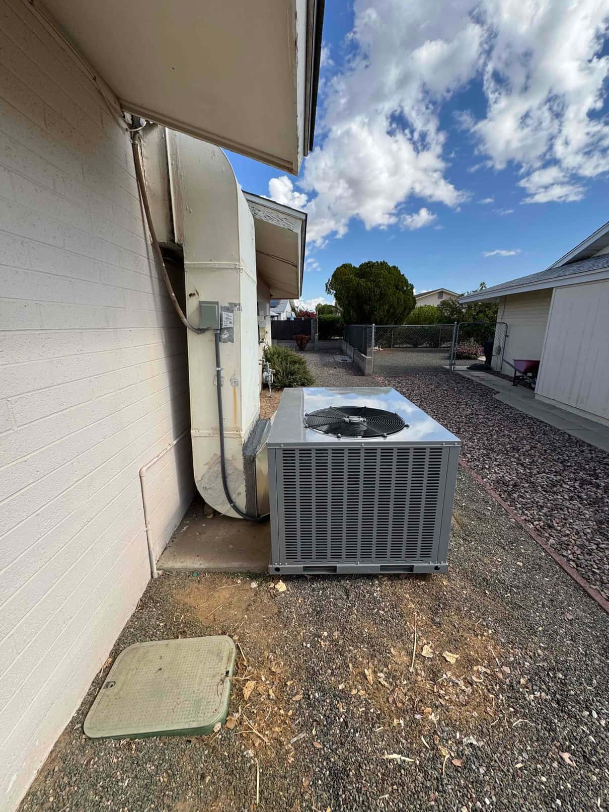 New package unit set outdoors on ground beside duct connection and electrical disconnect at residential installation site.