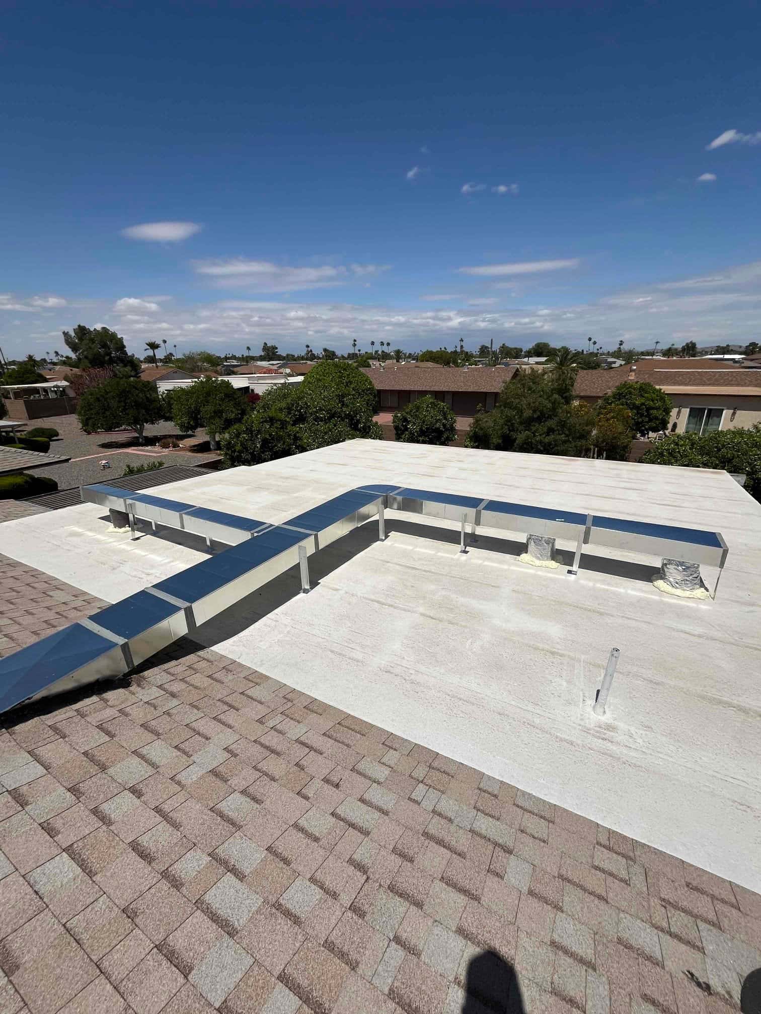 New rooftop ductwork runs on supports over a coated flat roof, with sealed penetrations and adjacent shingle roof area.