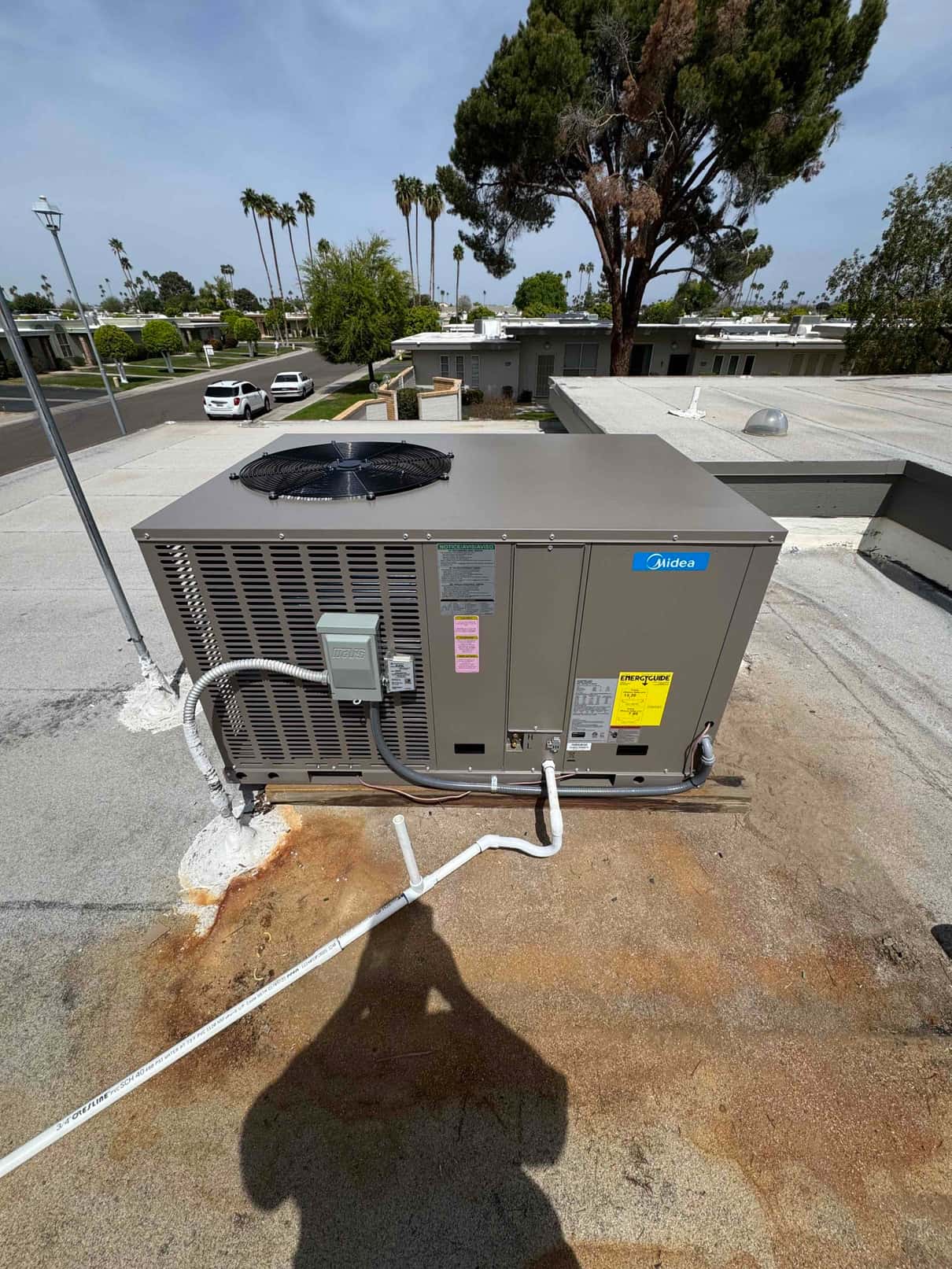 New rooftop package unit set on curb with electrical whip, condensate drain piping, and secured refrigerant line connections.