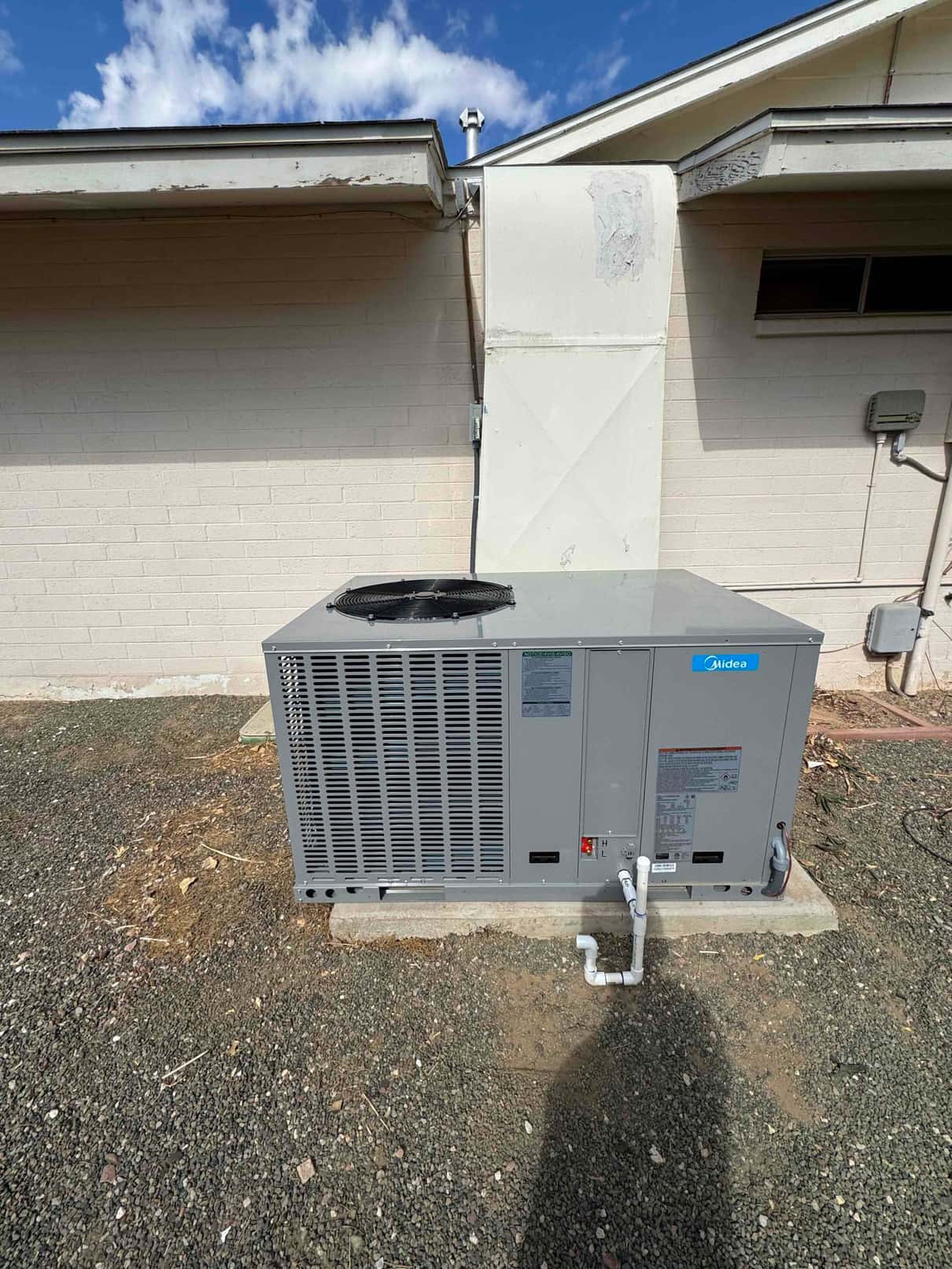 New rooftop-style package unit installed on a concrete pad with connected condensate drain and duct transition to the building.