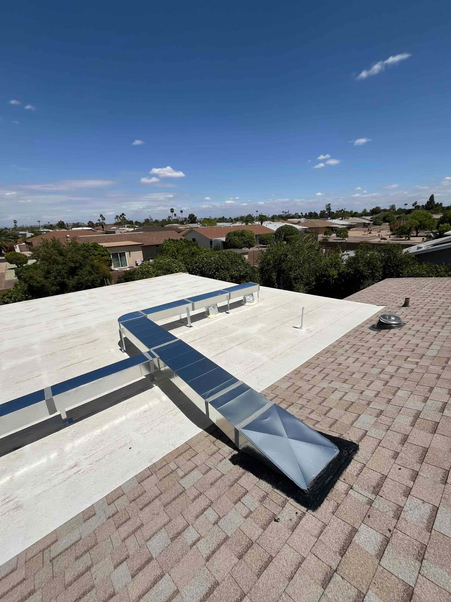 New sheet-metal rooftop ductwork installed and sealed at the shingle transition, with multiple runs supported across the flat roof.