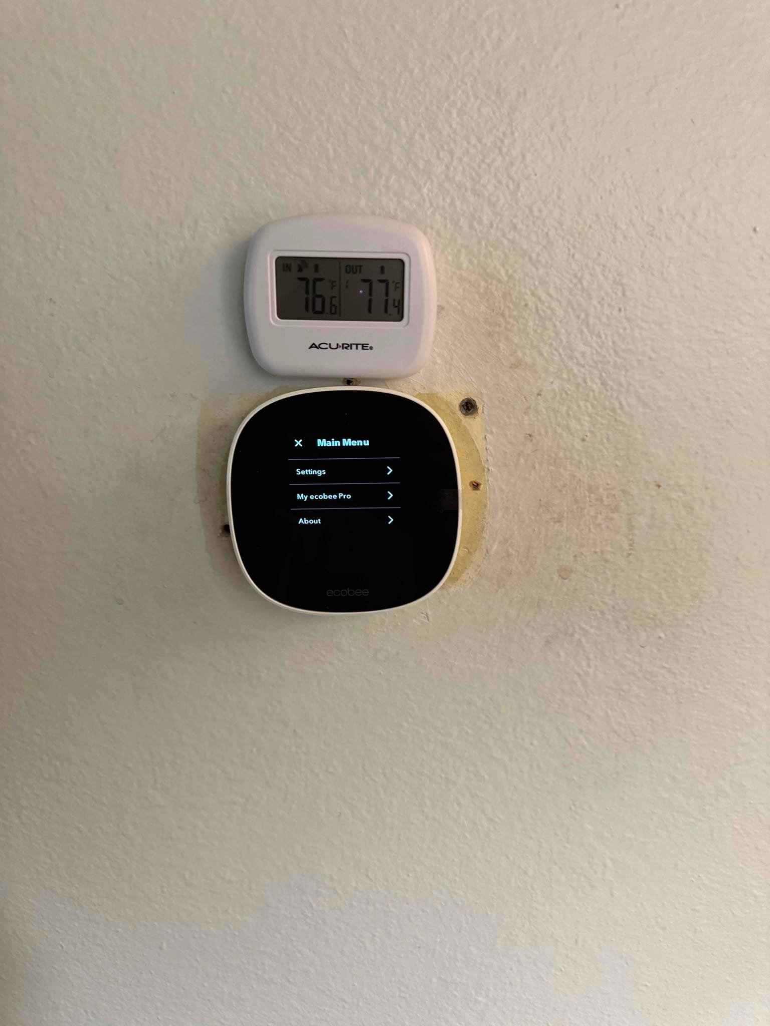 New smart thermostat mounted on the wall beneath a digital indoor and outdoor temperature display during commissioning.