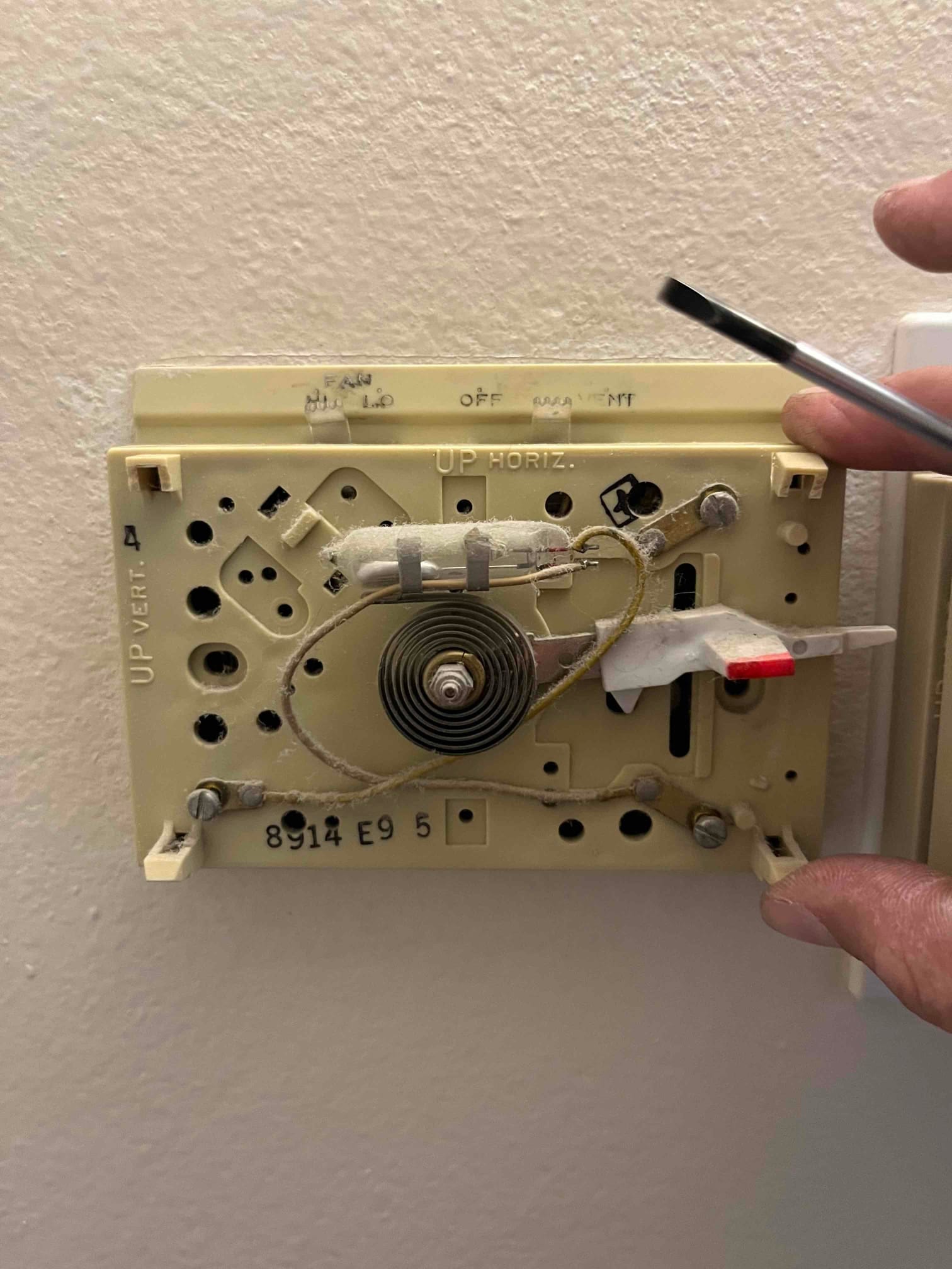 Old mechanical thermostat base exposed on the wall with wiring and bimetal coil visible during replacement.