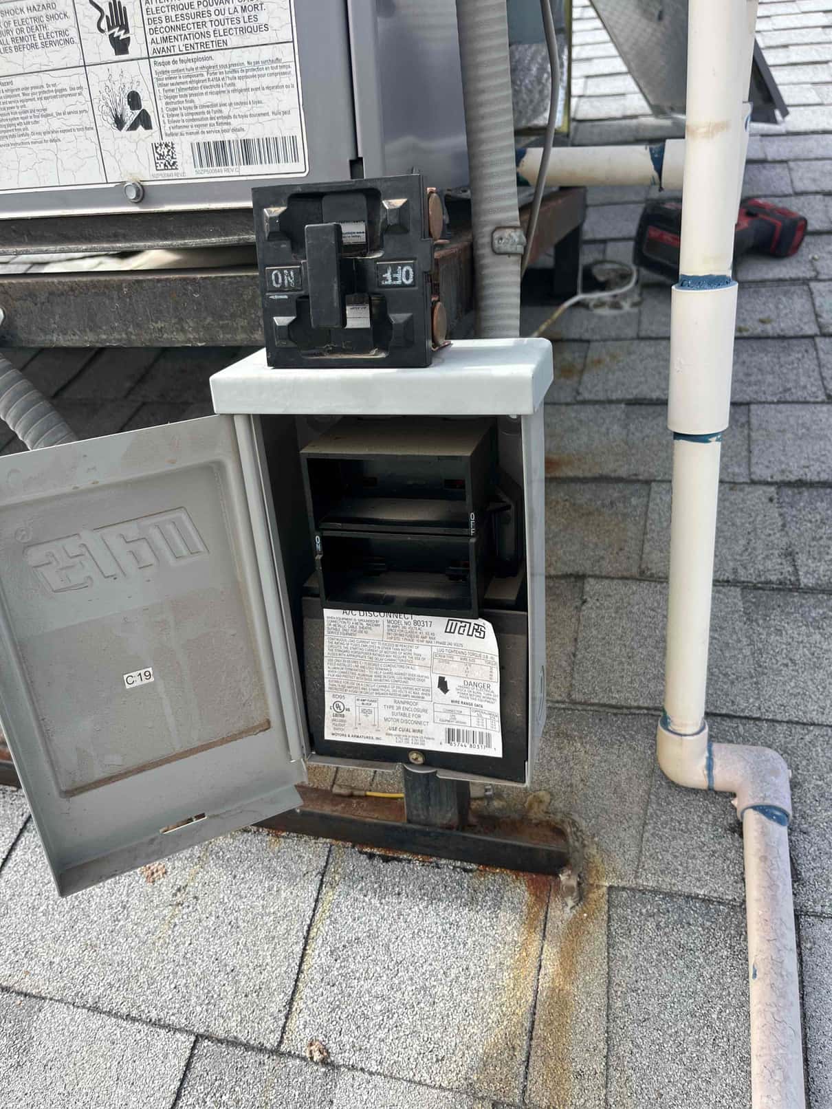 Outdoor AC disconnect box open, showing pull-out fuse block and wiring beside the condenser on a rooftop.