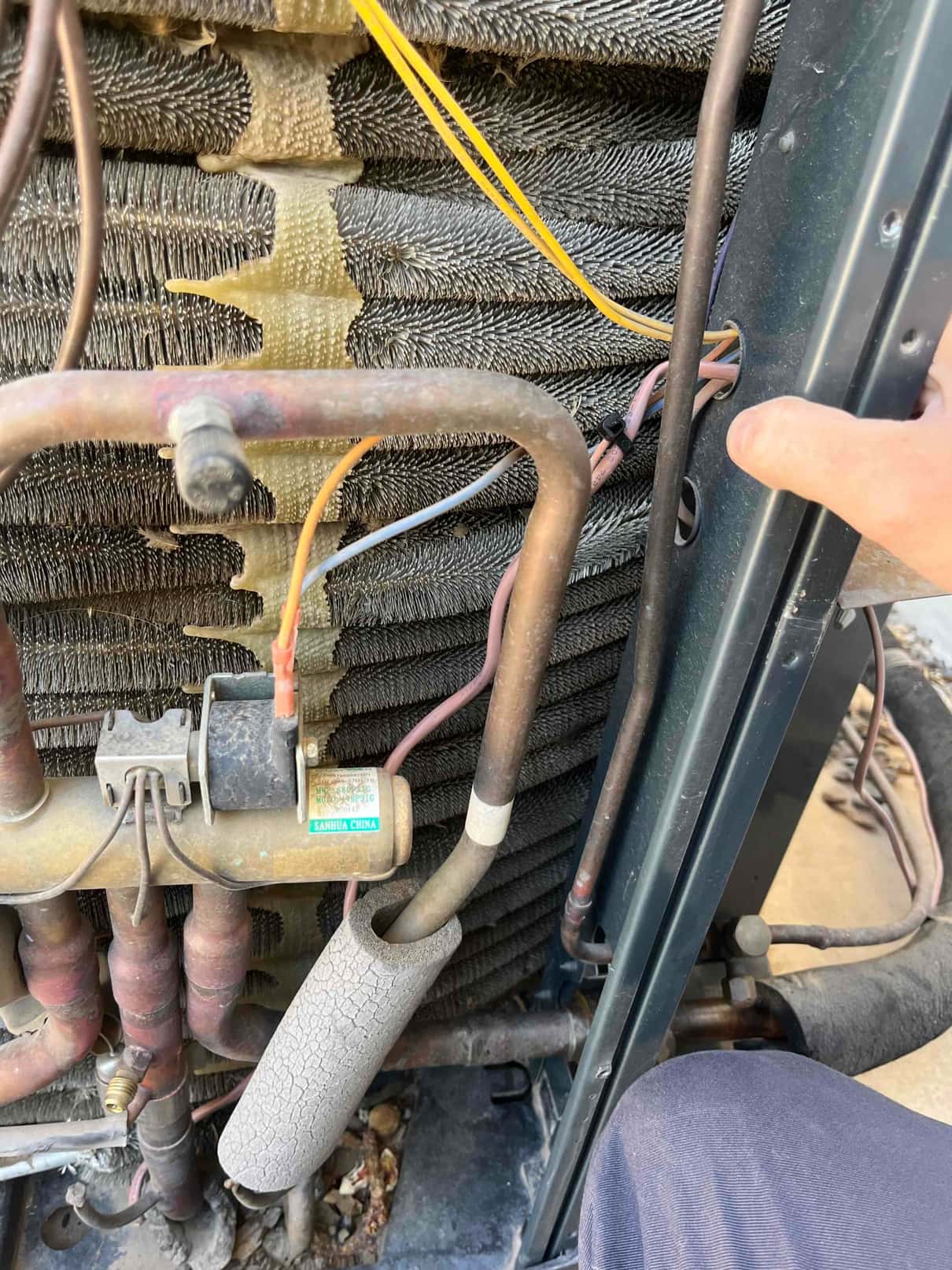 Outdoor condenser coil with exposed tubing, pressure switch wiring connections, and deteriorated insulation on the suction line.