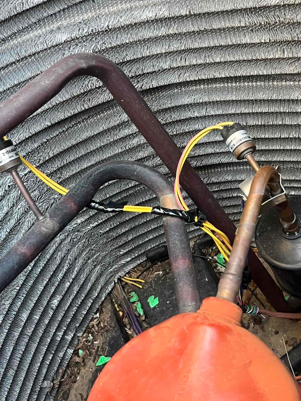 Outdoor condenser interior shows repaired yellow control wiring with connectors and tape routed near copper refrigerant lines and filter-drier.