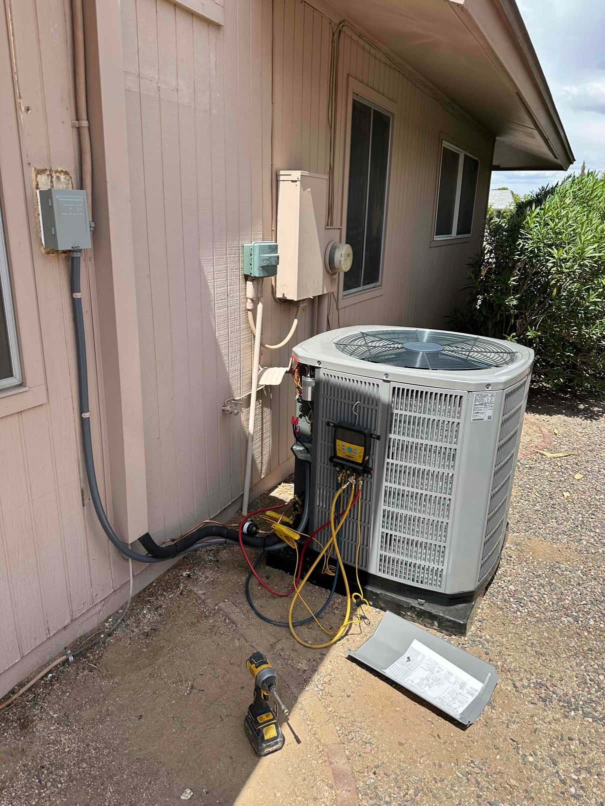 Outdoor condenser set on a level pad with new line set, electrical whip, and manifold gauges connected during commissioning.