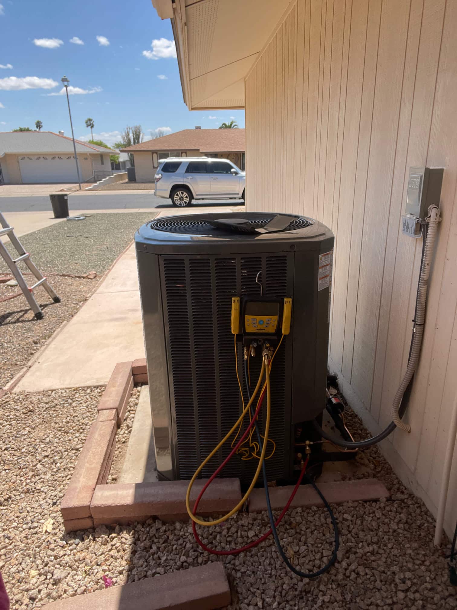 Outdoor heat pump condenser set on a level pad with digital manifold gauges connected to the service ports during commissioning.