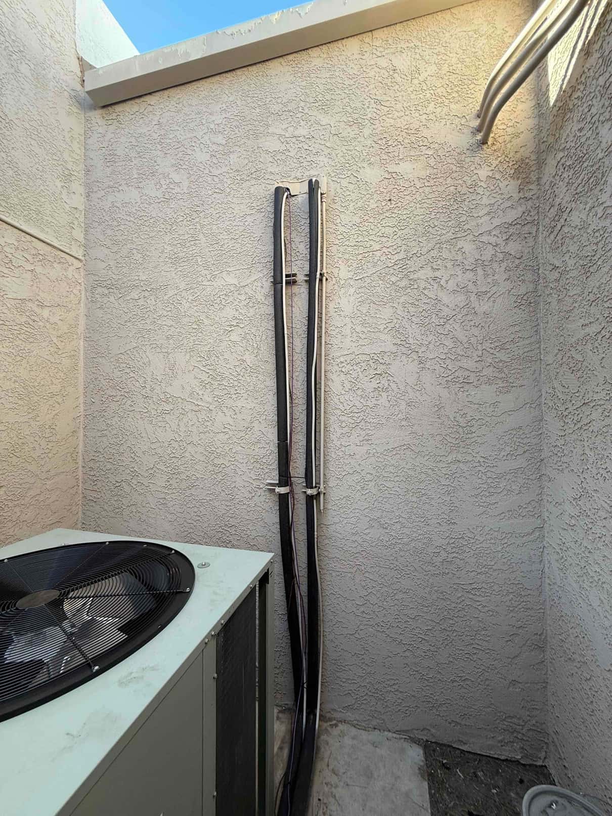 Outdoor heat pump condenser set on a pad with insulated refrigerant lines and electrical conduit secured neatly along the wall.