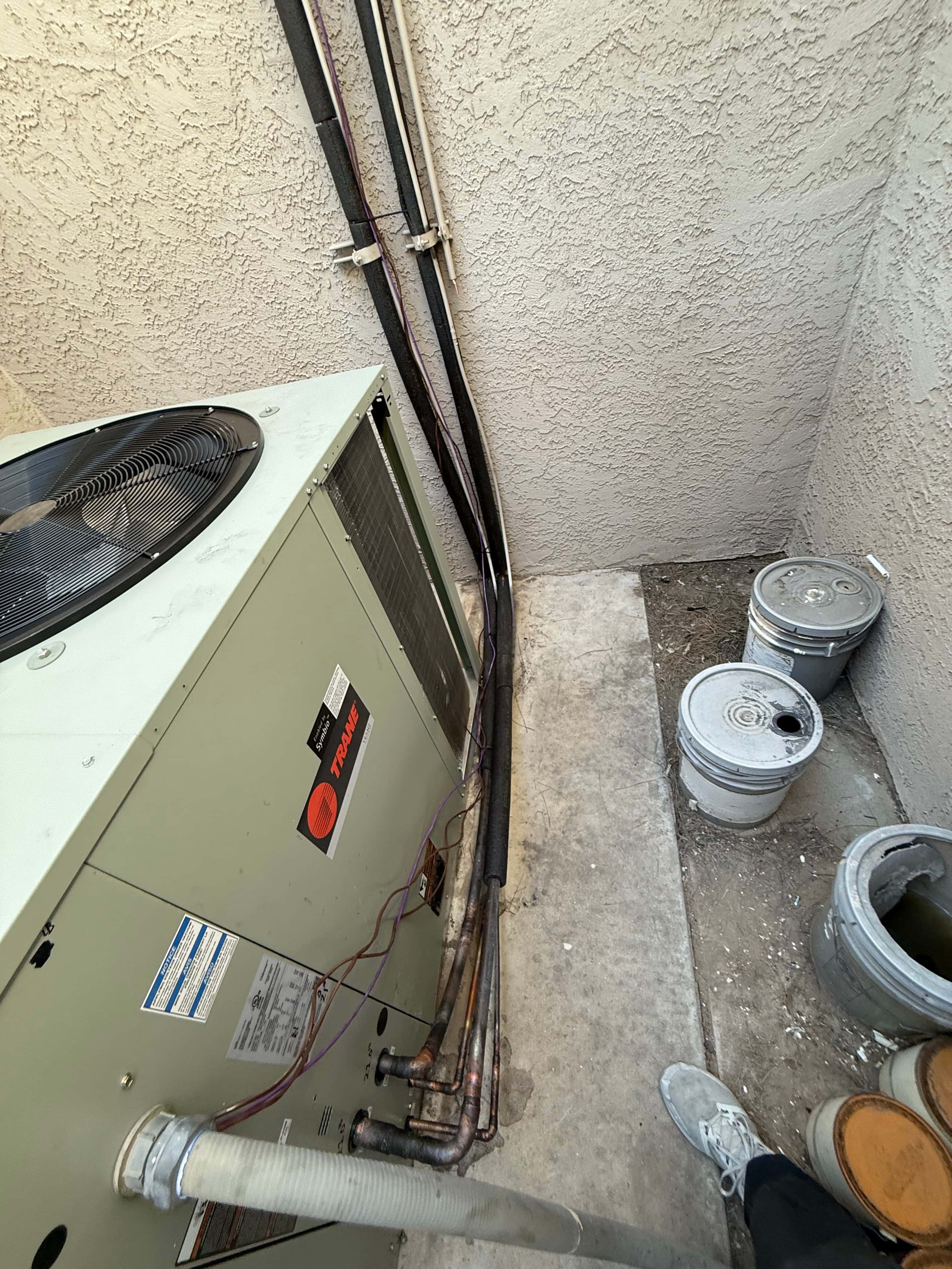 Packaged HVAC unit set outdoors with insulated refrigerant lines, control wiring, and condensate drain routed along the wall.