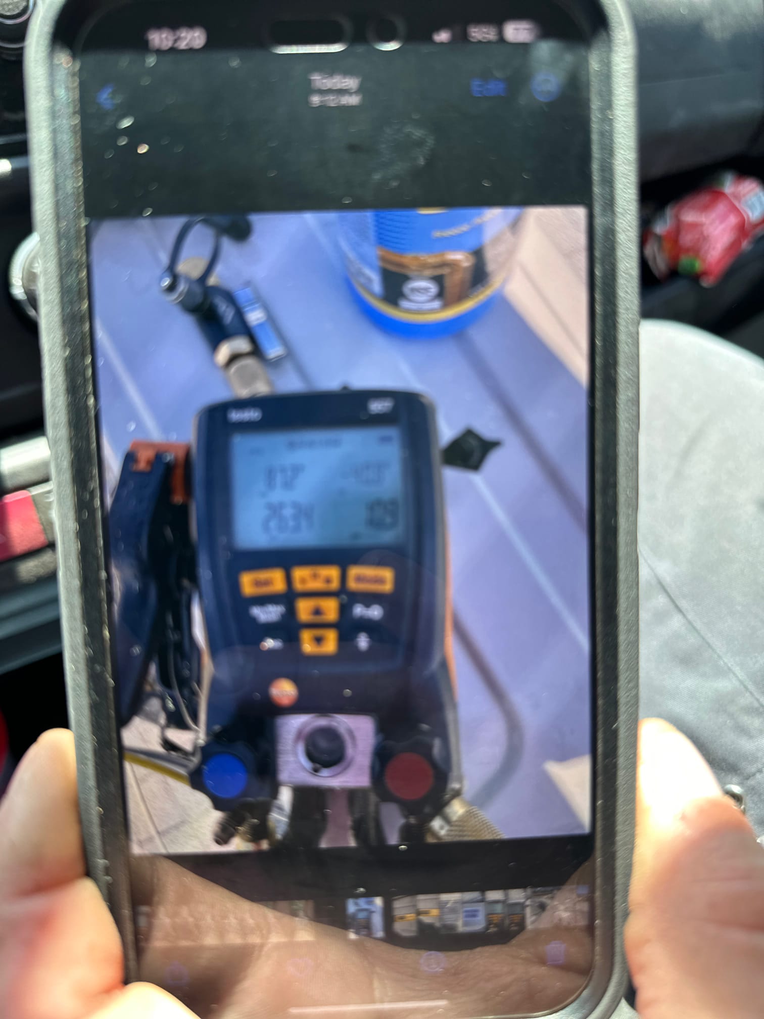Phone screen shows a digital manifold gauge with hoses connected during HVAC work, but the display readings are not legible.