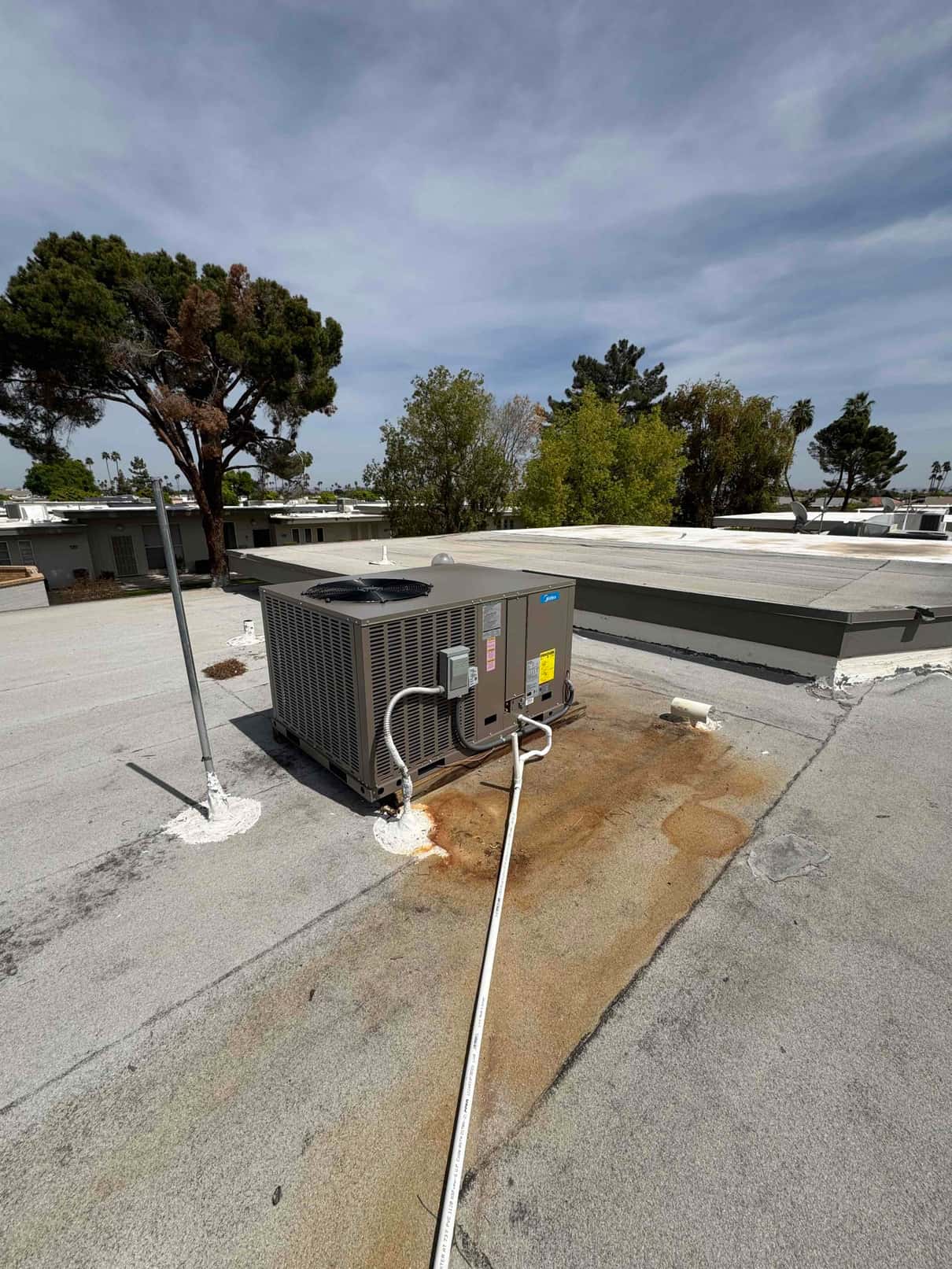 Rooftop package HVAC unit installed on a flat roof with electrical conduit and condensate drain routed across the surface.