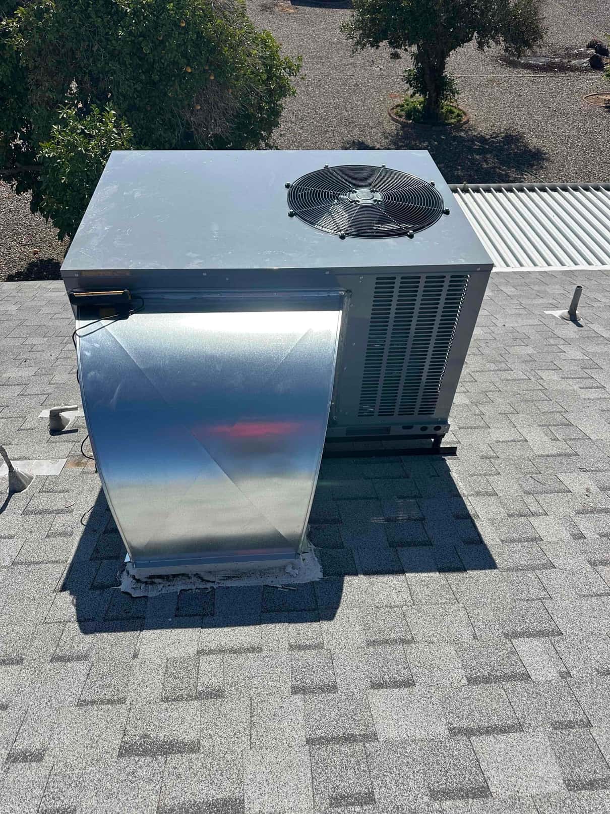 Rooftop package HVAC unit installed on shingles with new sheet-metal curb adapter and sealed base flashing.