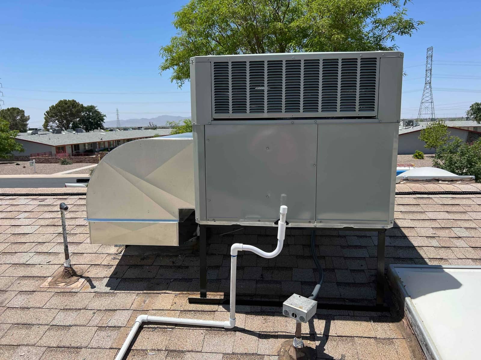 Rooftop packaged HVAC unit set on stands with new sheet-metal duct connection, condensate drain, and electrical whip visible.