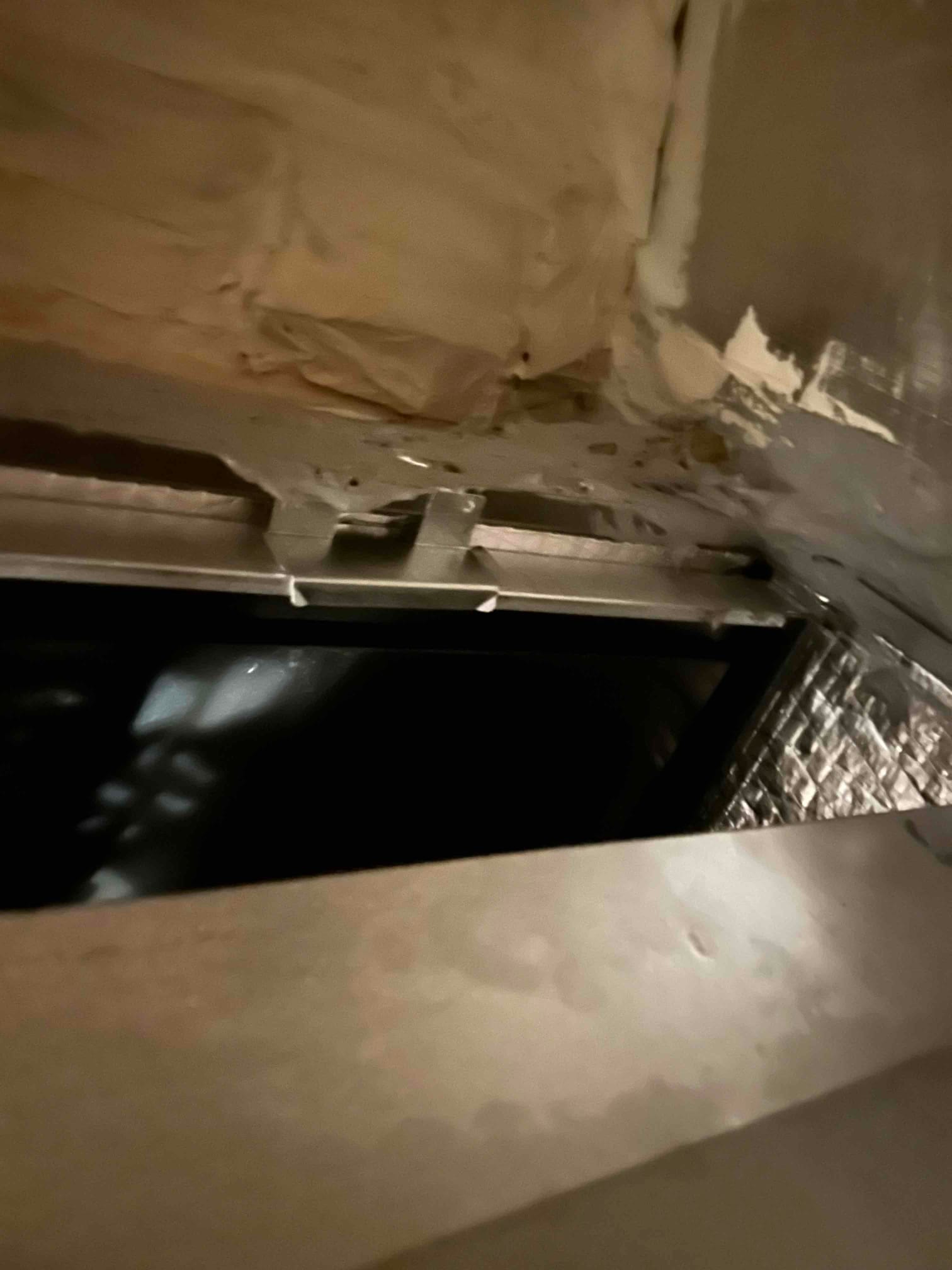 Sheet-metal duct connection with mastic-sealed seams and insulation visible at the plenum transition.