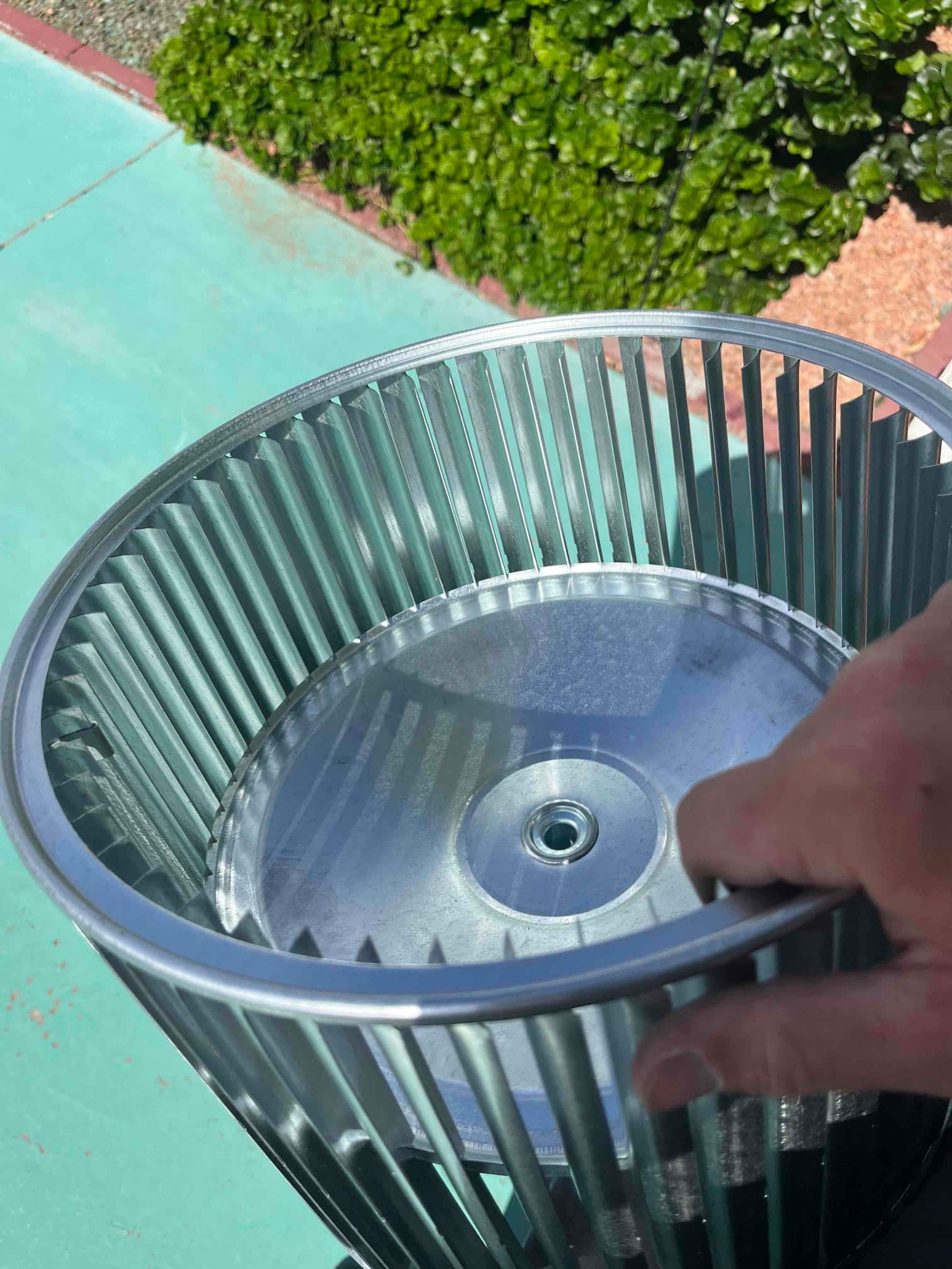 Technician hand holds a new metal blower wheel assembly outdoors, showing clean, undamaged fins and central hub.