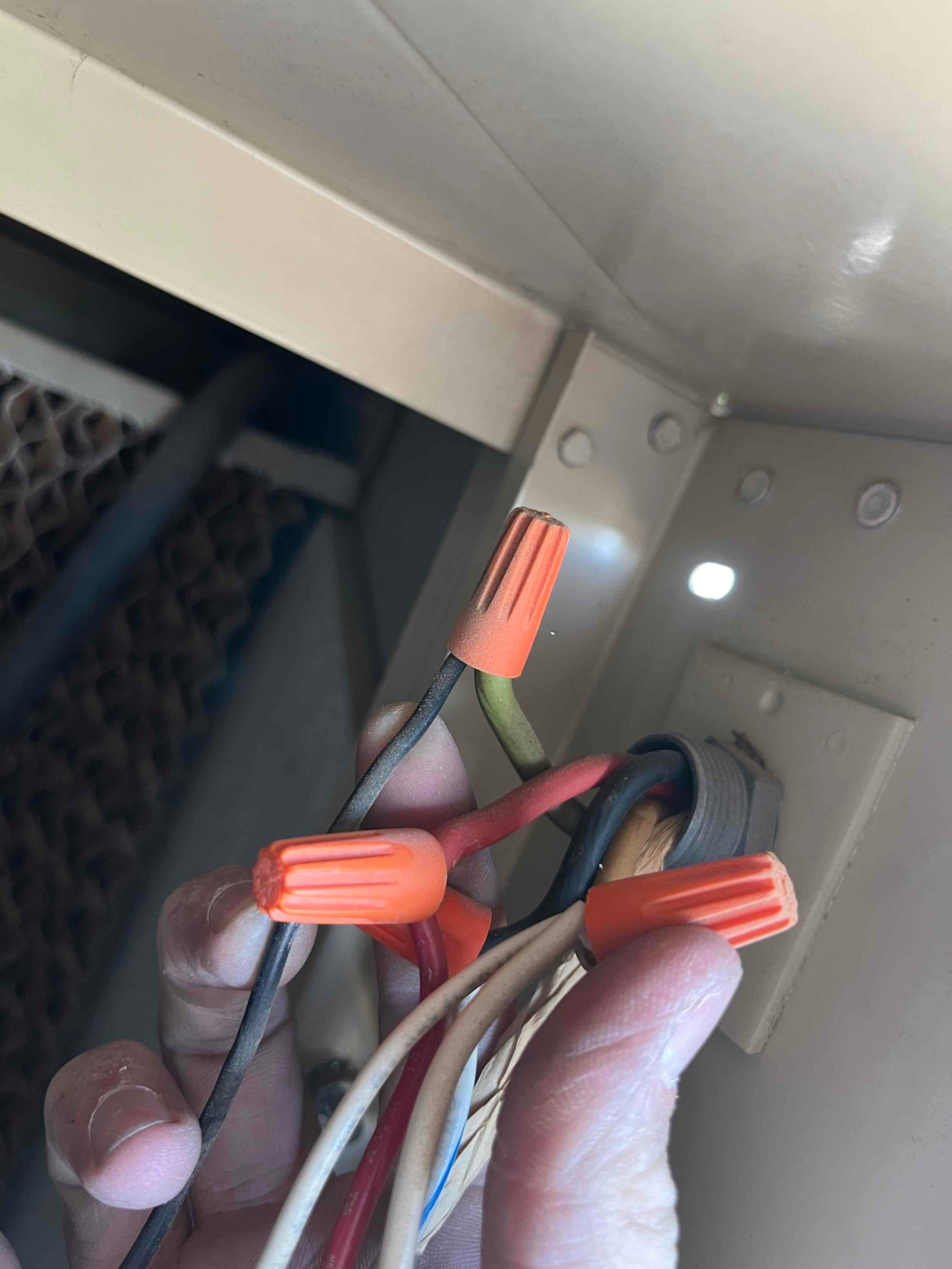 Technician holds bundled control wires with orange wire nuts inside the unit cabinet next to a grommeted entry point.