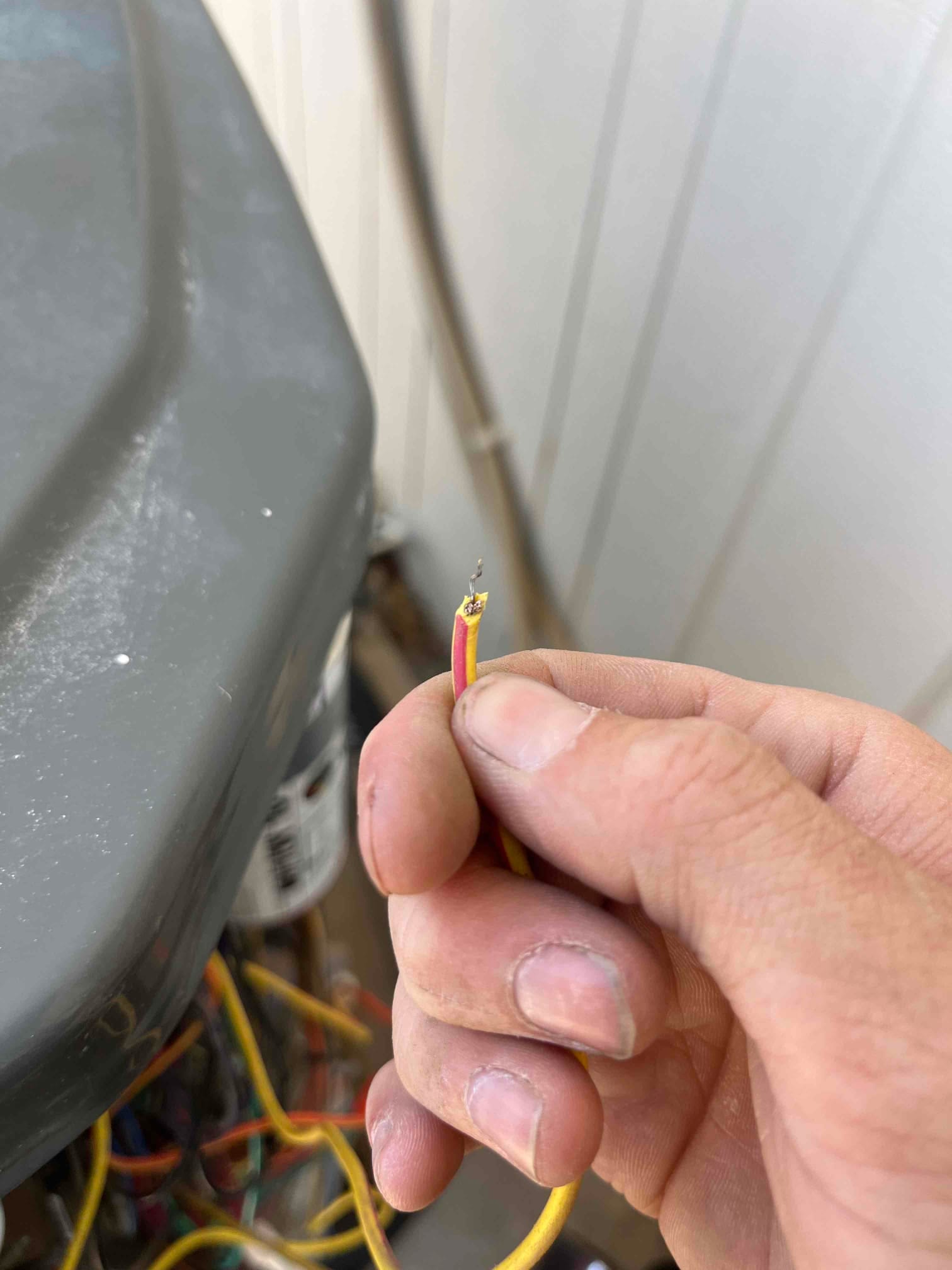 Technician holds a stripped two-conductor control wire at an outdoor condenser, exposing bare copper for repair.