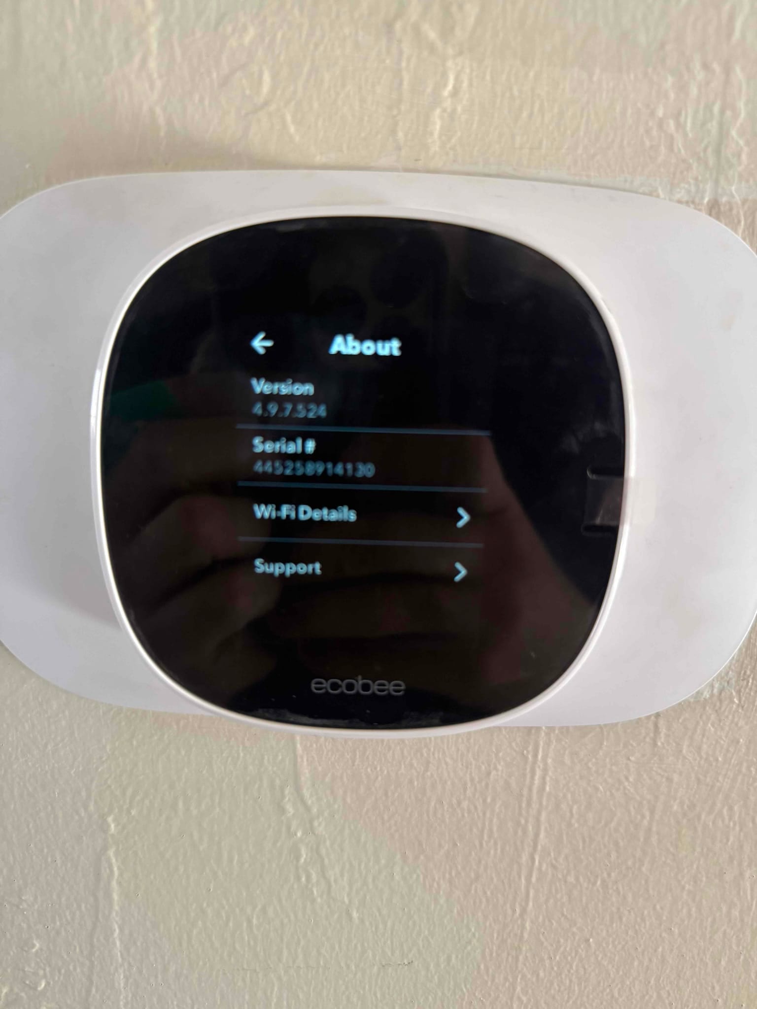Thermostat mounted on wall displaying the About menu with software version and menu options for Wi‑Fi details and support.