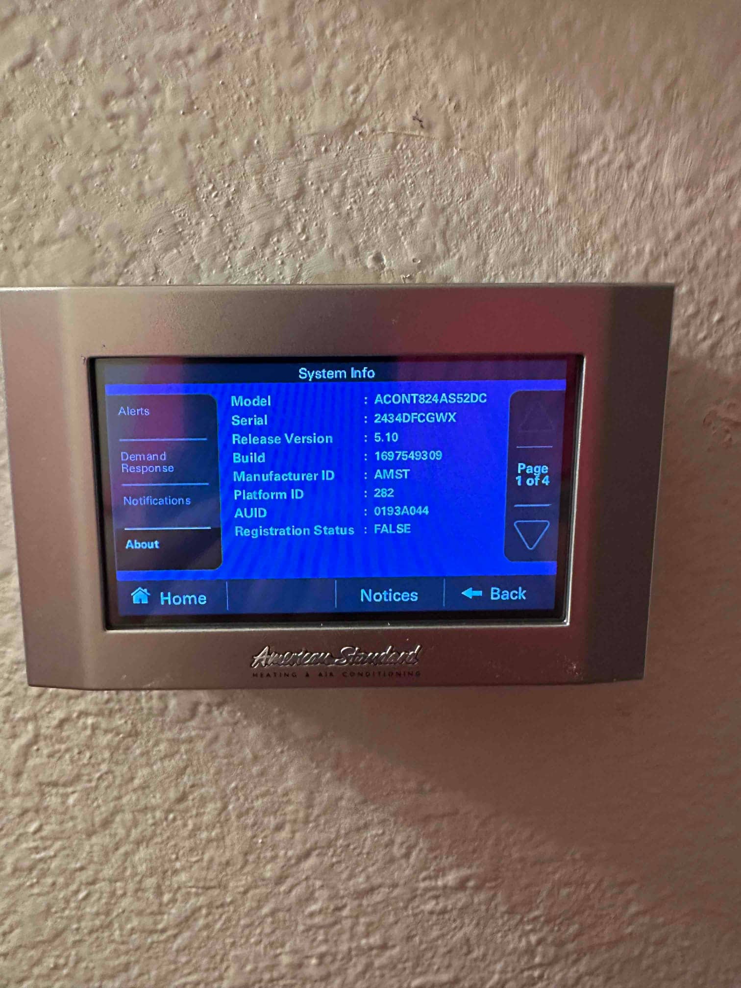 Touchscreen thermostat mounted on interior wall displaying system information and menu options after installation.