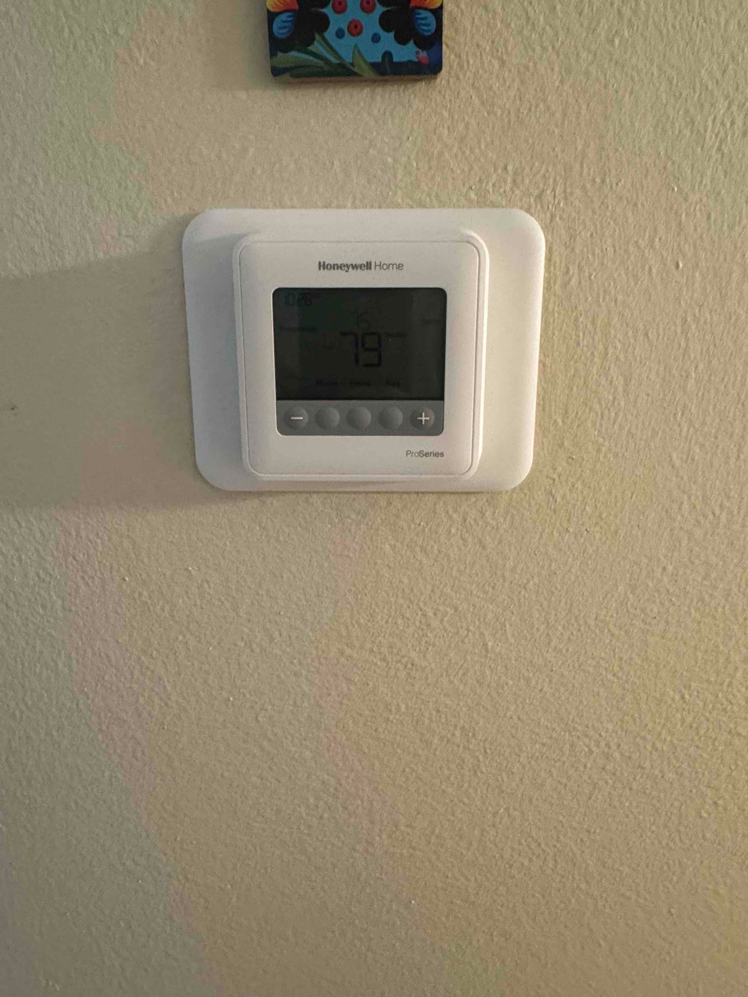 Wall-mounted digital thermostat installed and powered on, displaying room temperature and control buttons for system operation.
