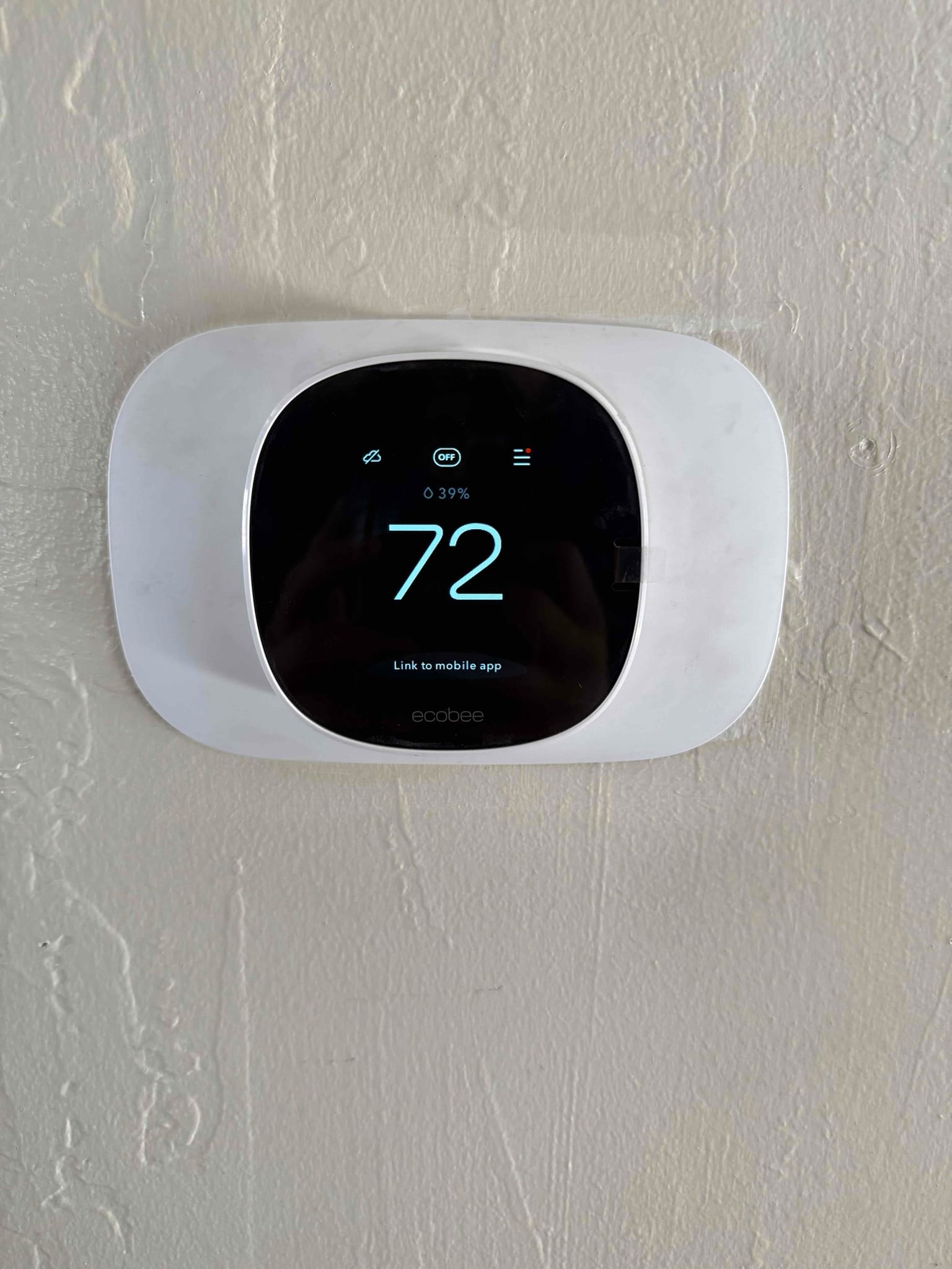 Wall-mounted smart thermostat installed and powered on, displaying 72 degrees with system status icons and menu indicators.