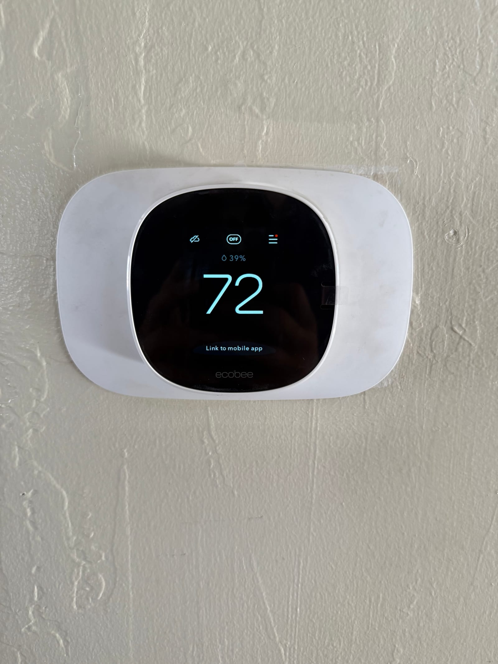 Wall-mounted smart thermostat installed and powered on, displaying an indoor temperature of 72 degrees with system status indicators.