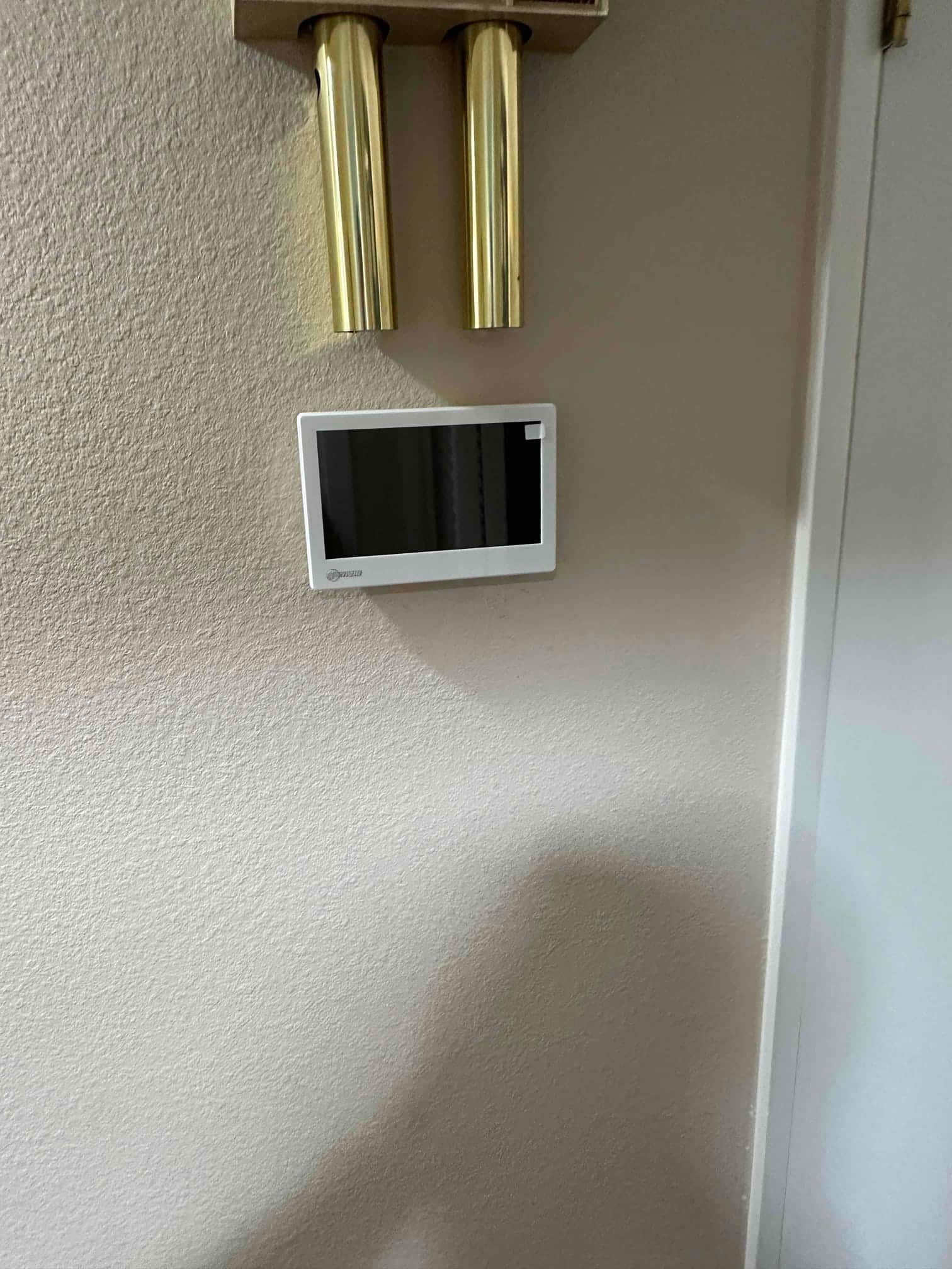 Wall-mounted touchscreen thermostat installed near an interior door, screen off, showing clean finish and proper placement.