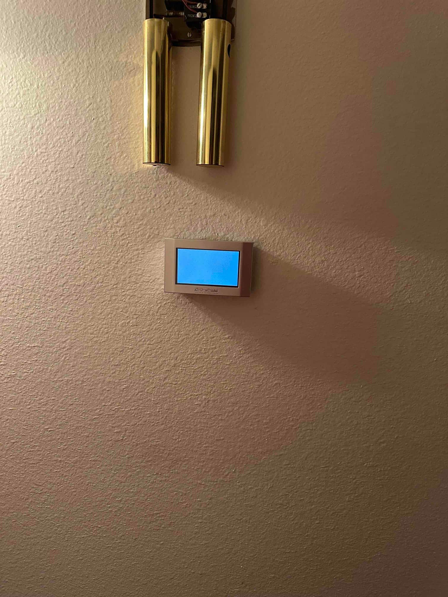 Wall-mounted touchscreen thermostat installed and powered on, shown beneath a decorative wall sconce.