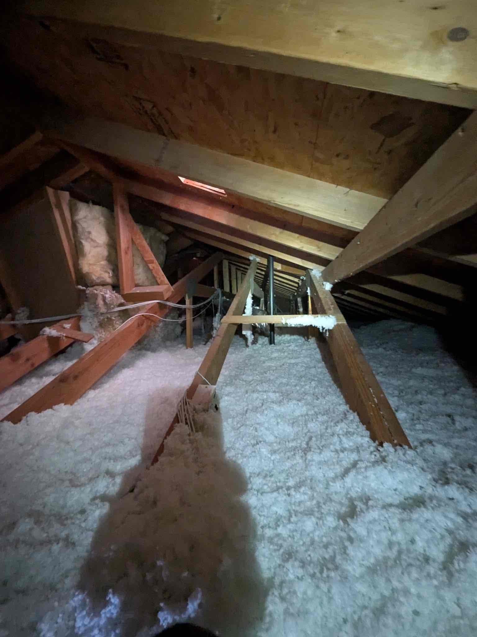 Attic space with new blown-in insulation around roof trusses and a narrow service walkway leading toward the equipment location.