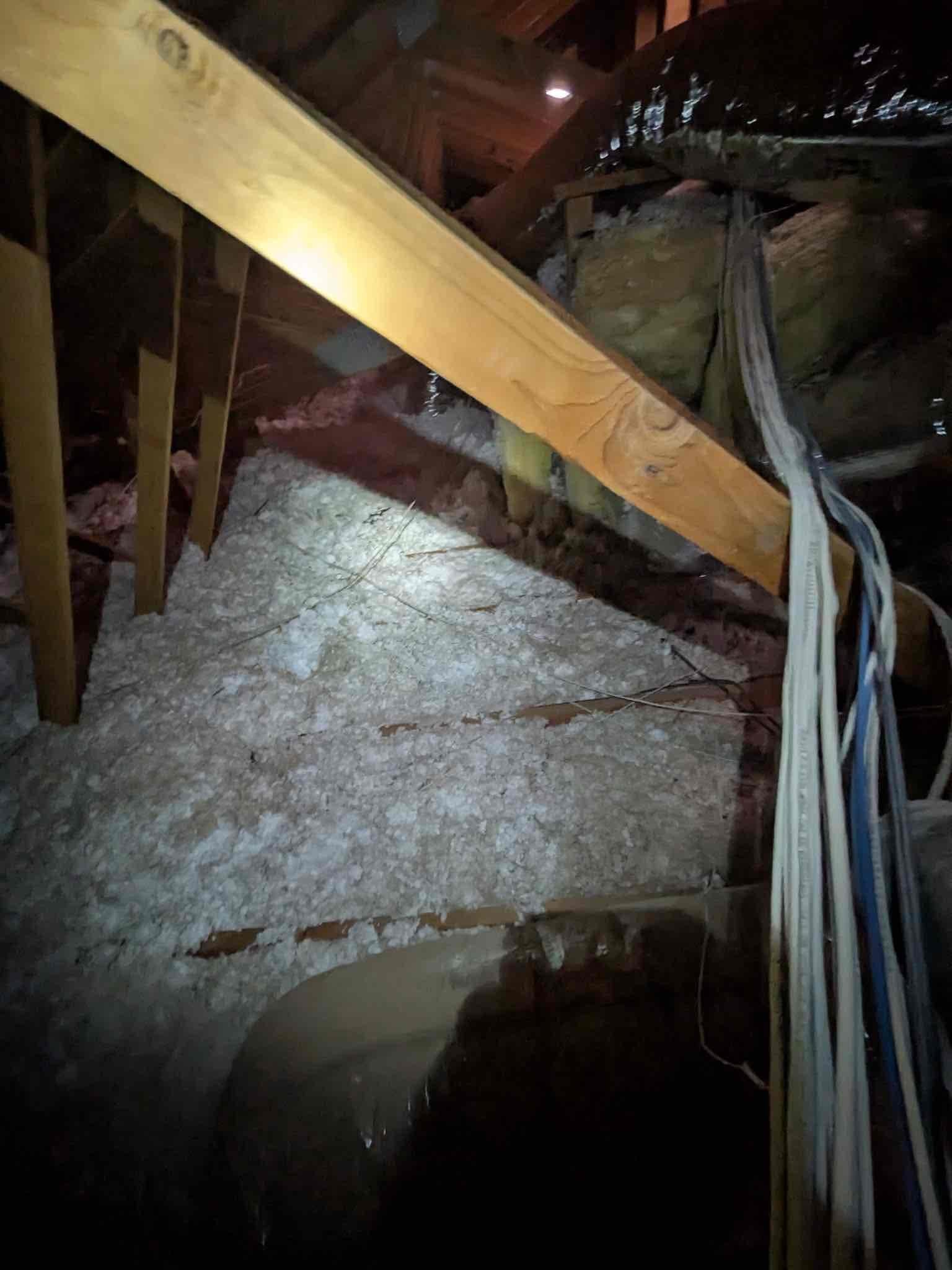Attic view showing blown-in insulation, roof framing, and bundled low-voltage control cables routed alongside insulated ductwork.