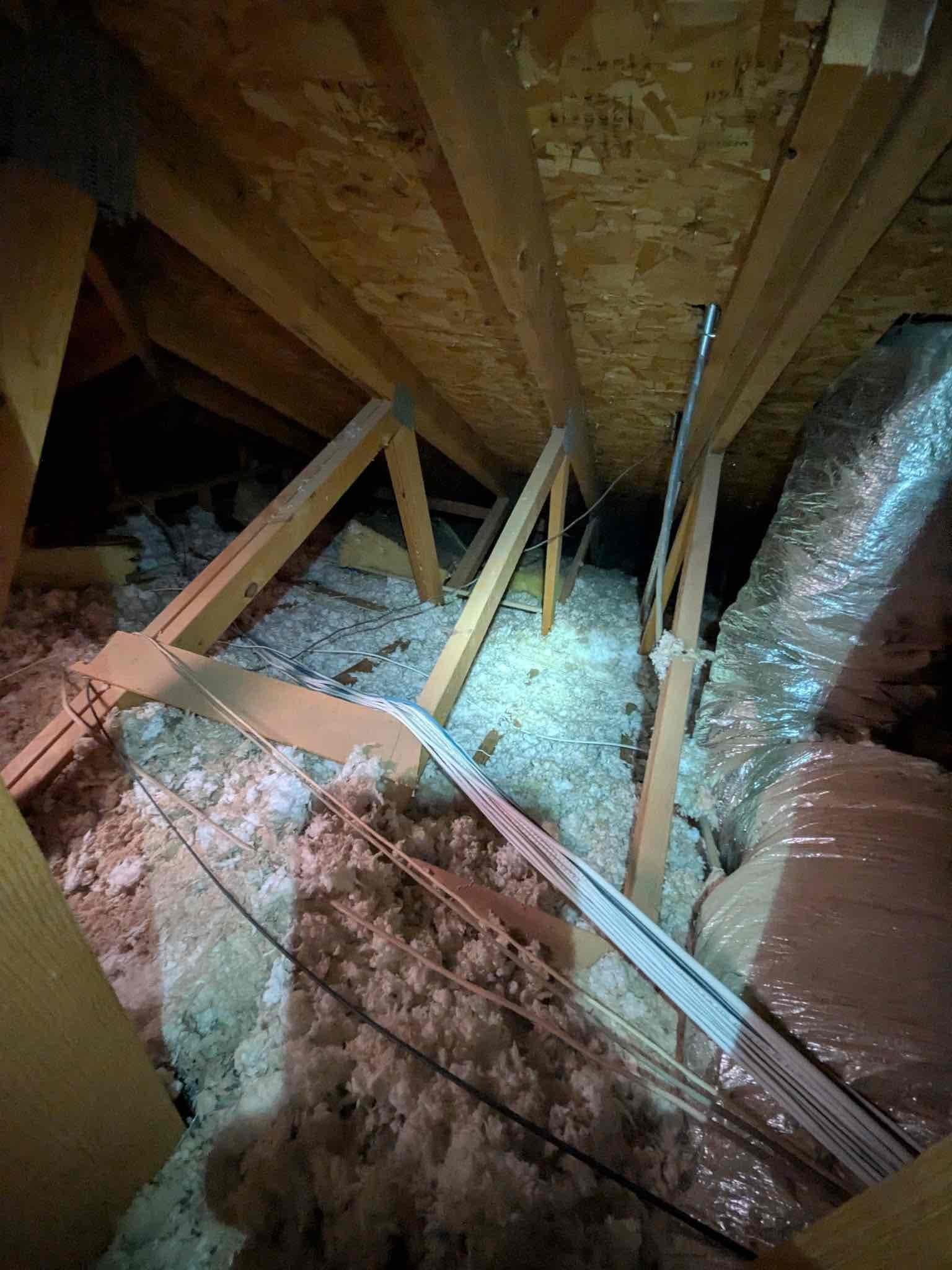 Attic view showing insulated flexible duct, low-voltage control wiring, and blown-in insulation routed across roof trusses.