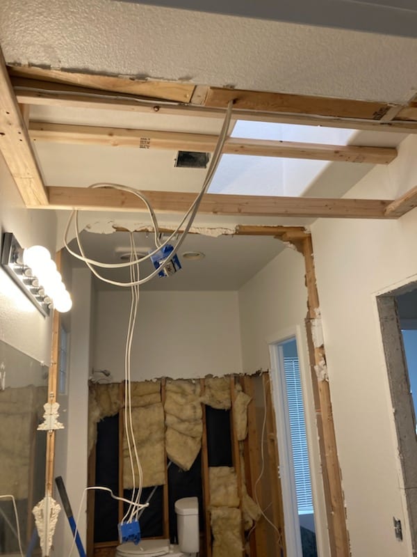 Bathroom ceiling opened with exposed framing, insulation, and duct opening visible during supply duct relocation work.