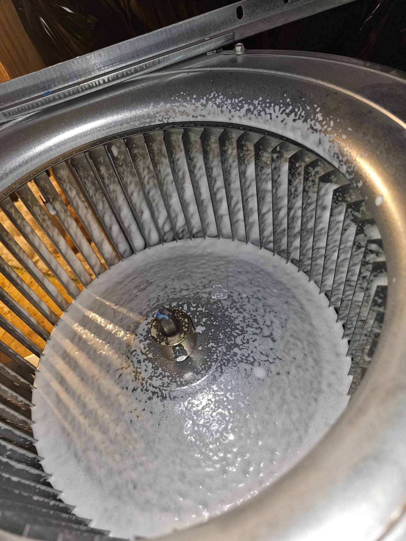 Blower wheel inside air handler coated with cleaning foam across blades and hub.