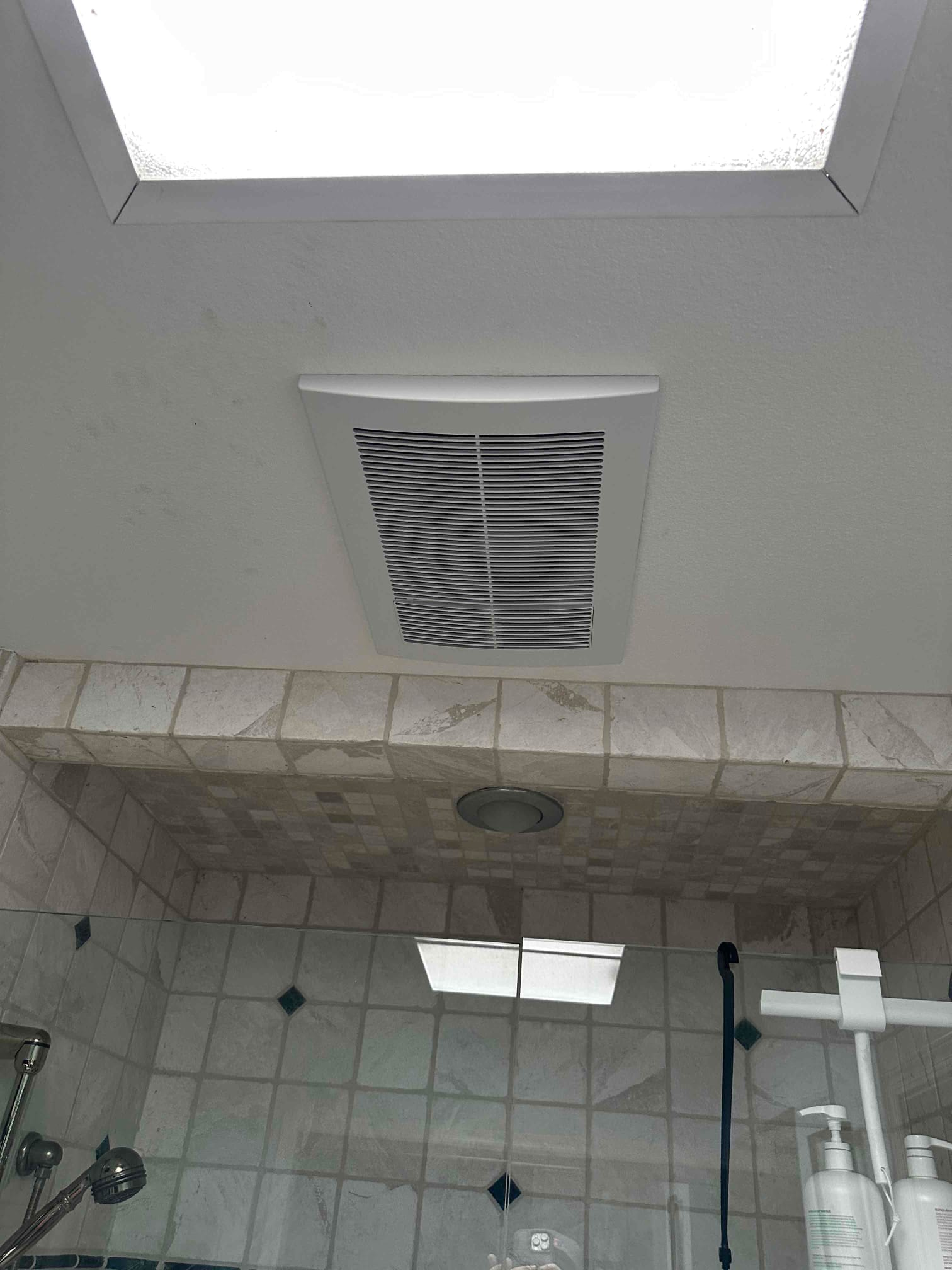 Ceiling-mounted HVAC grille installed above a tiled shower area, showing finished vent placement and surrounding surfaces.