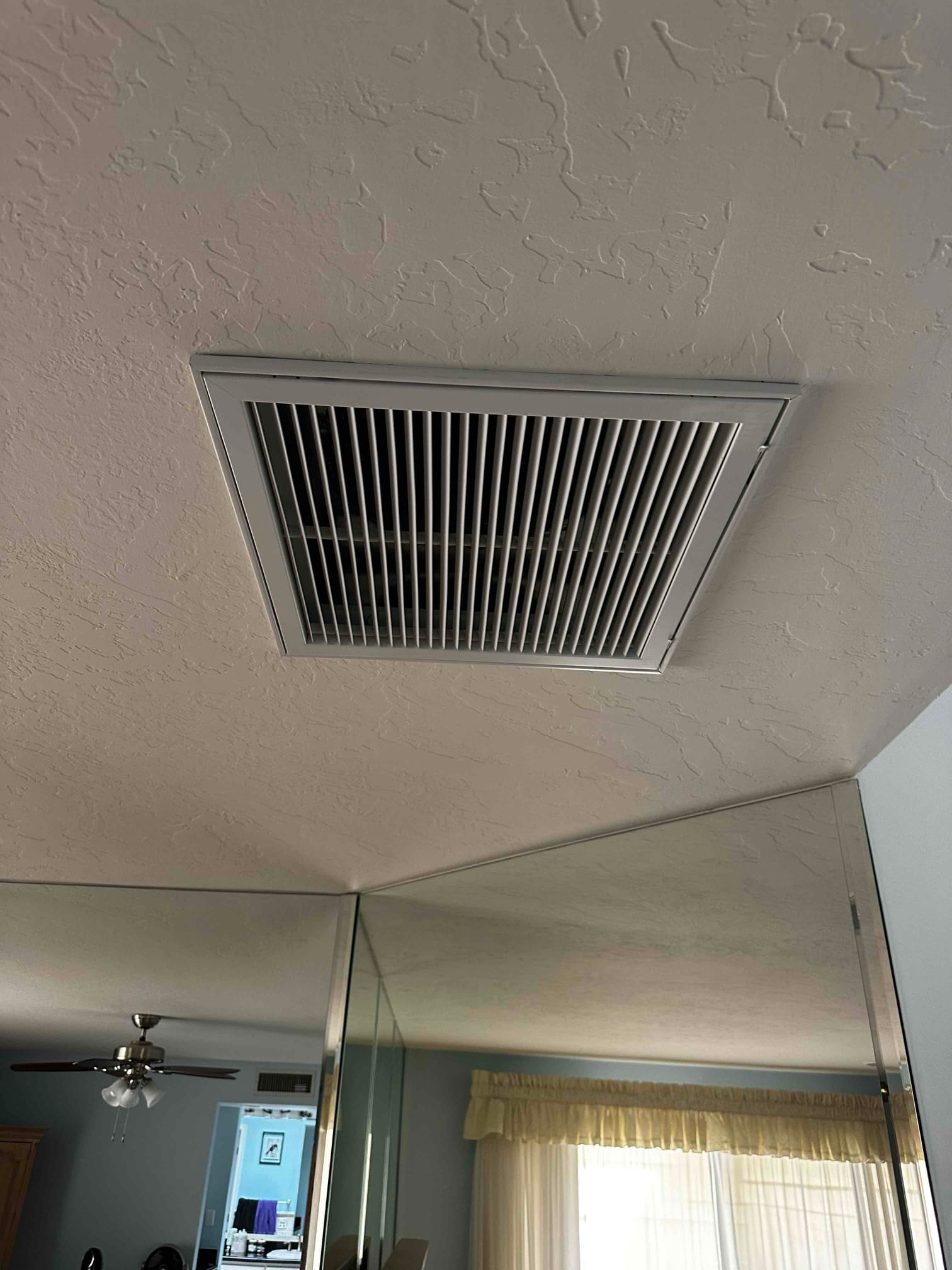 Ceiling-mounted return grille installed flush with textured drywall in a finished room, showing clean alignment and finished trim.