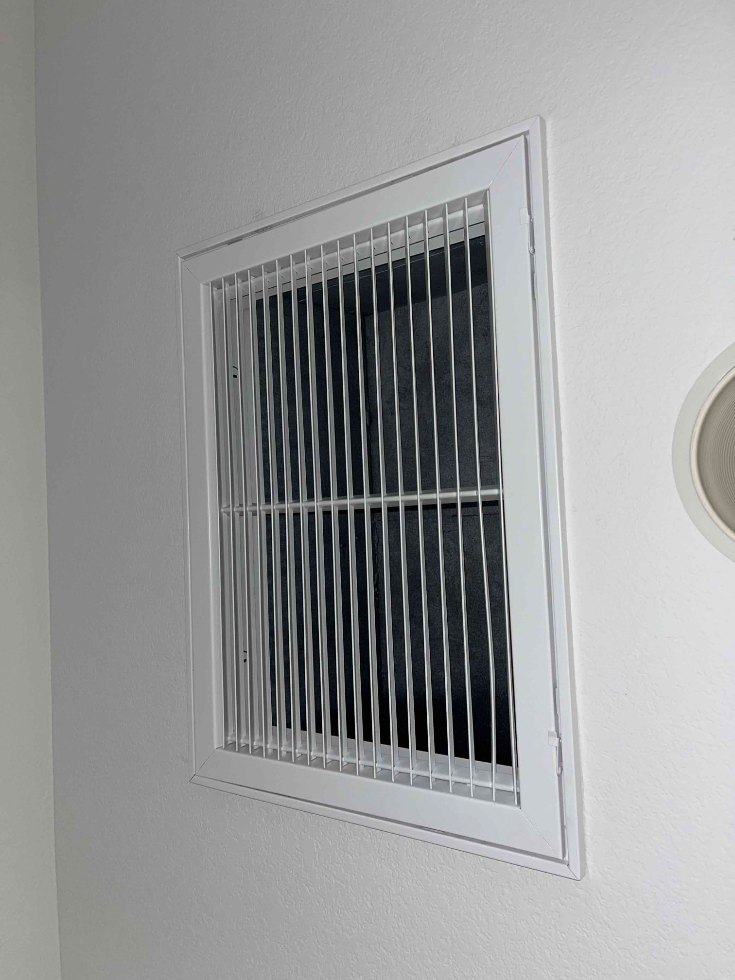 Ceiling return air grille with new white frame and clean louvers installed against a smooth painted surface.