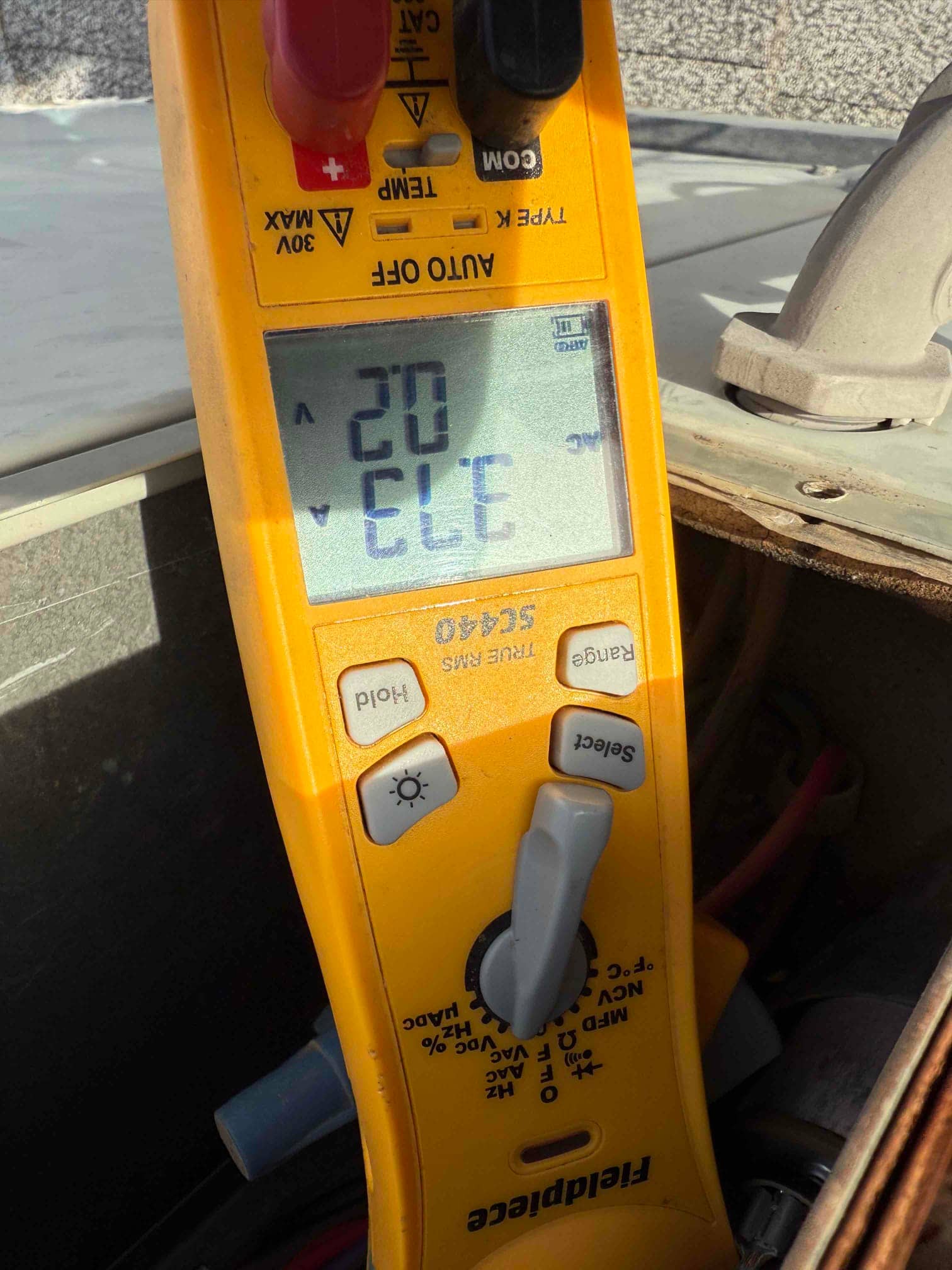 Clamp meter displays 20 A while measuring current on a single conductor inside the outdoor unit compartment.