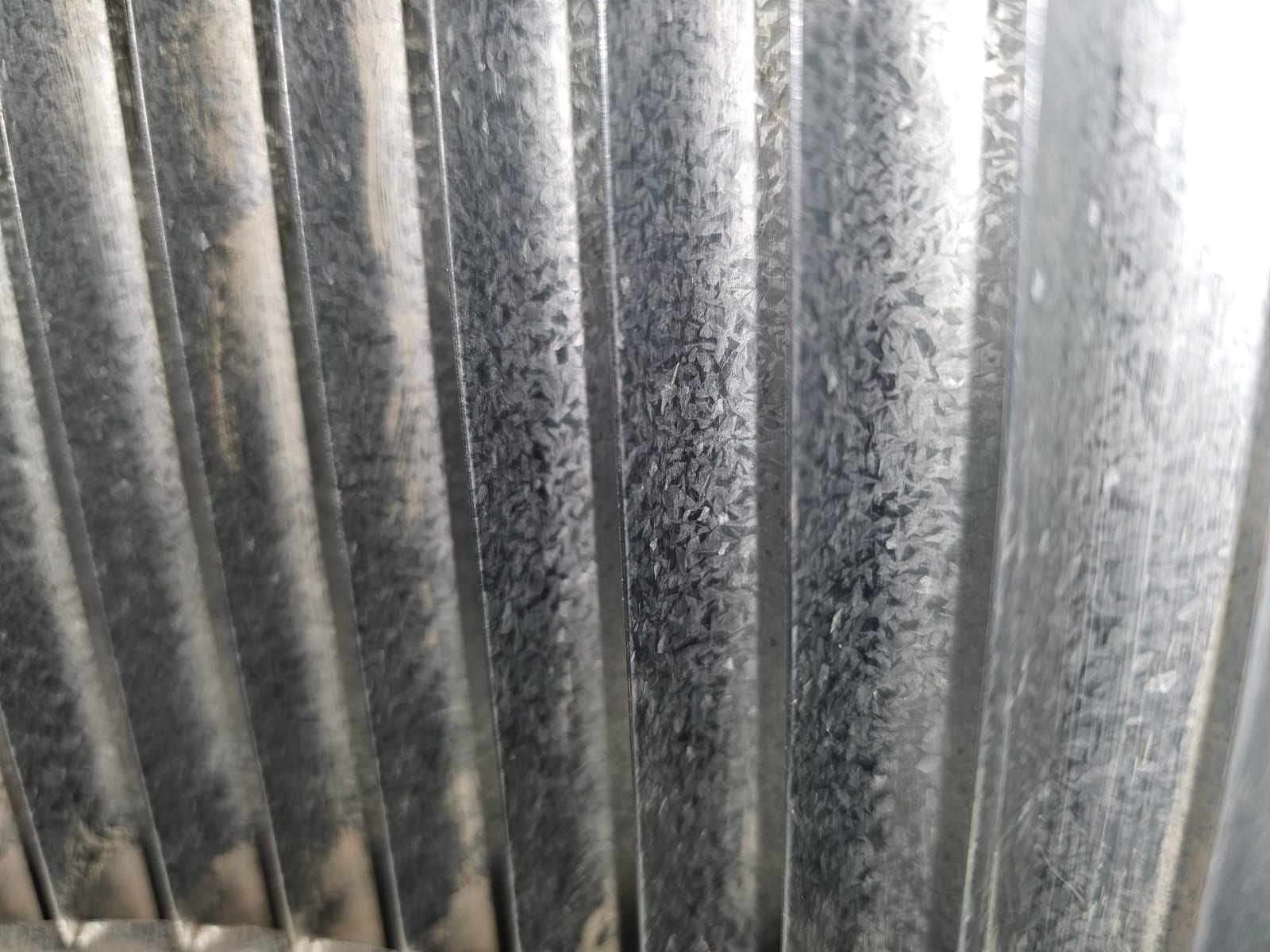 Close-up of corrugated galvanized sheet metal ducting with vertical ridges and reflective surface.