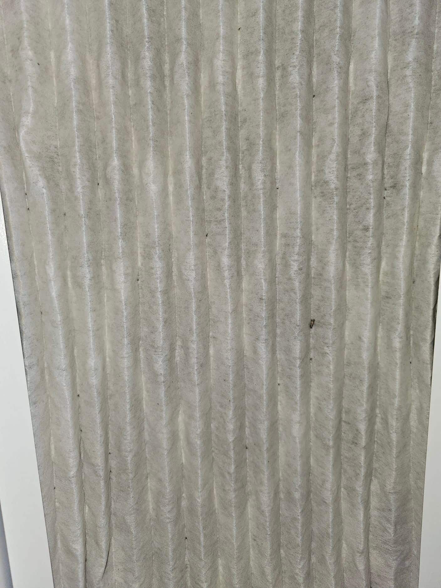 Close-up of a pleated HVAC air filter showing the filter media with small dust specks.