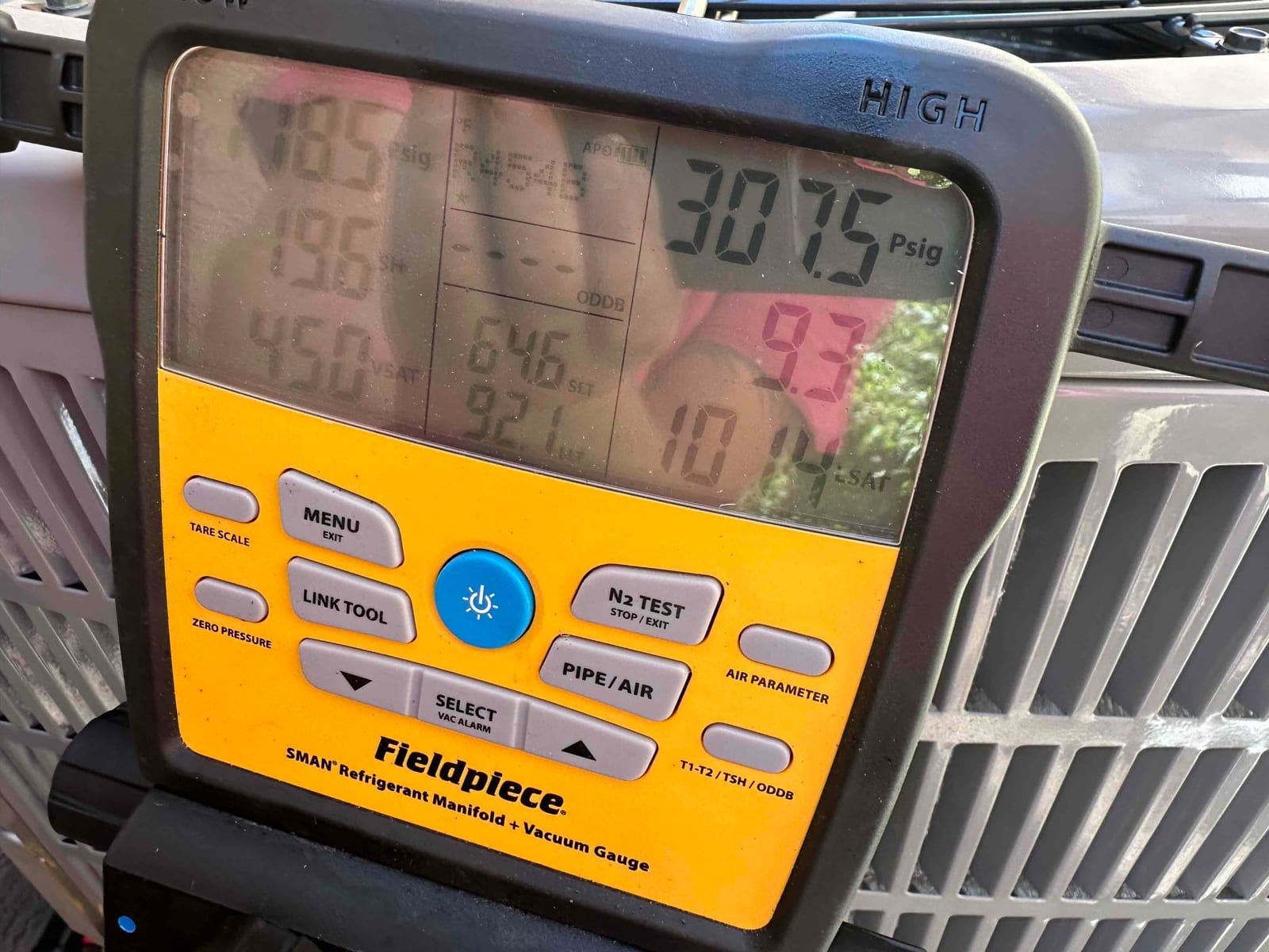 Digital manifold gauge on the outdoor unit shows operating refrigerant pressures with distinct high and low side readings during system commissioning.