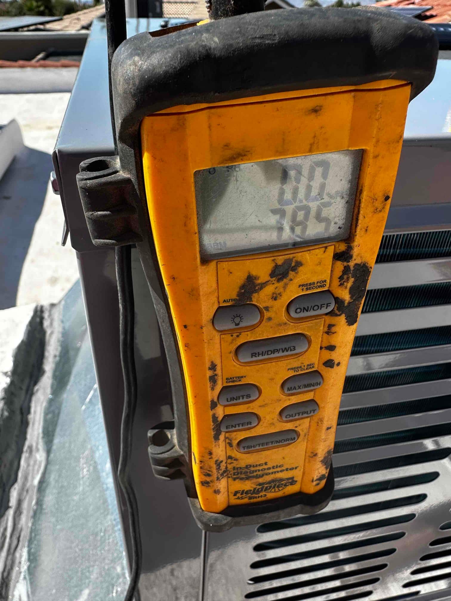 Digital thermometer probe attached at the outdoor unit shows an air temperature reading on the display during commissioning checks.