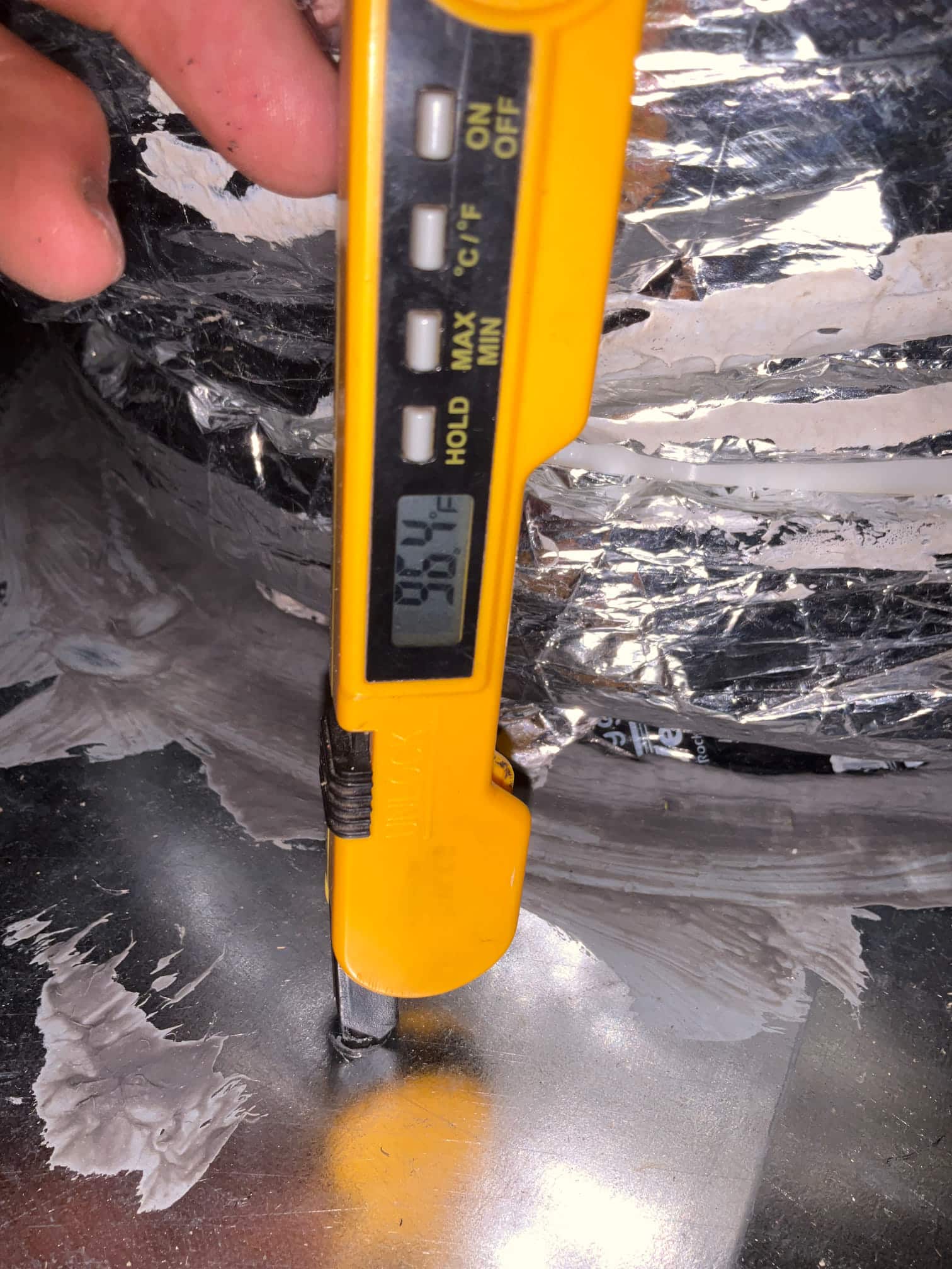 Digital thermometer probe inserted into ductwork reads 58.4°F, documenting supply air temperature after the evaporator.