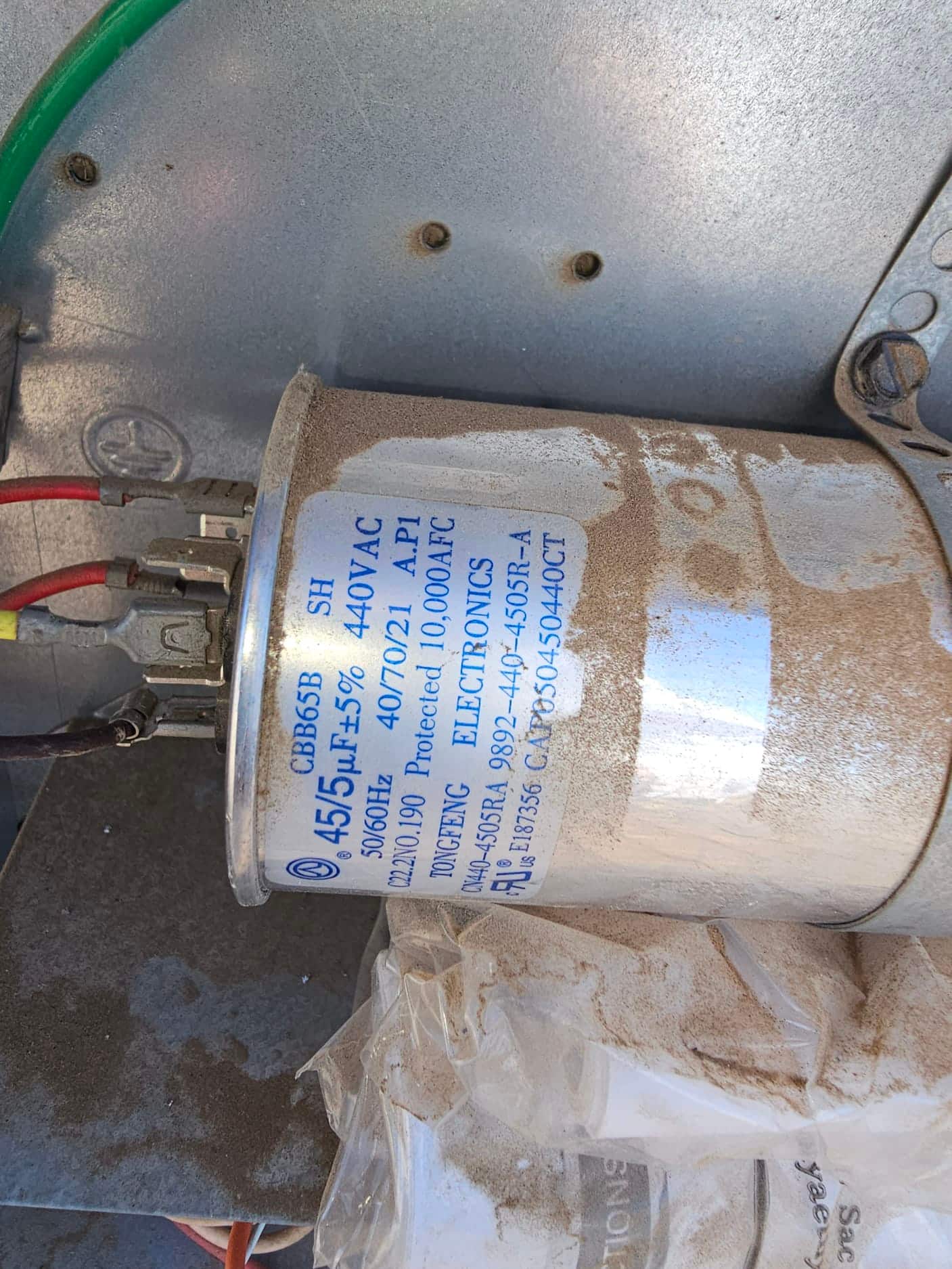 Dual-run capacitor labeled 45/5 μF ±5% 440VAC with connected wires, mounted inside the outdoor unit cabinet.