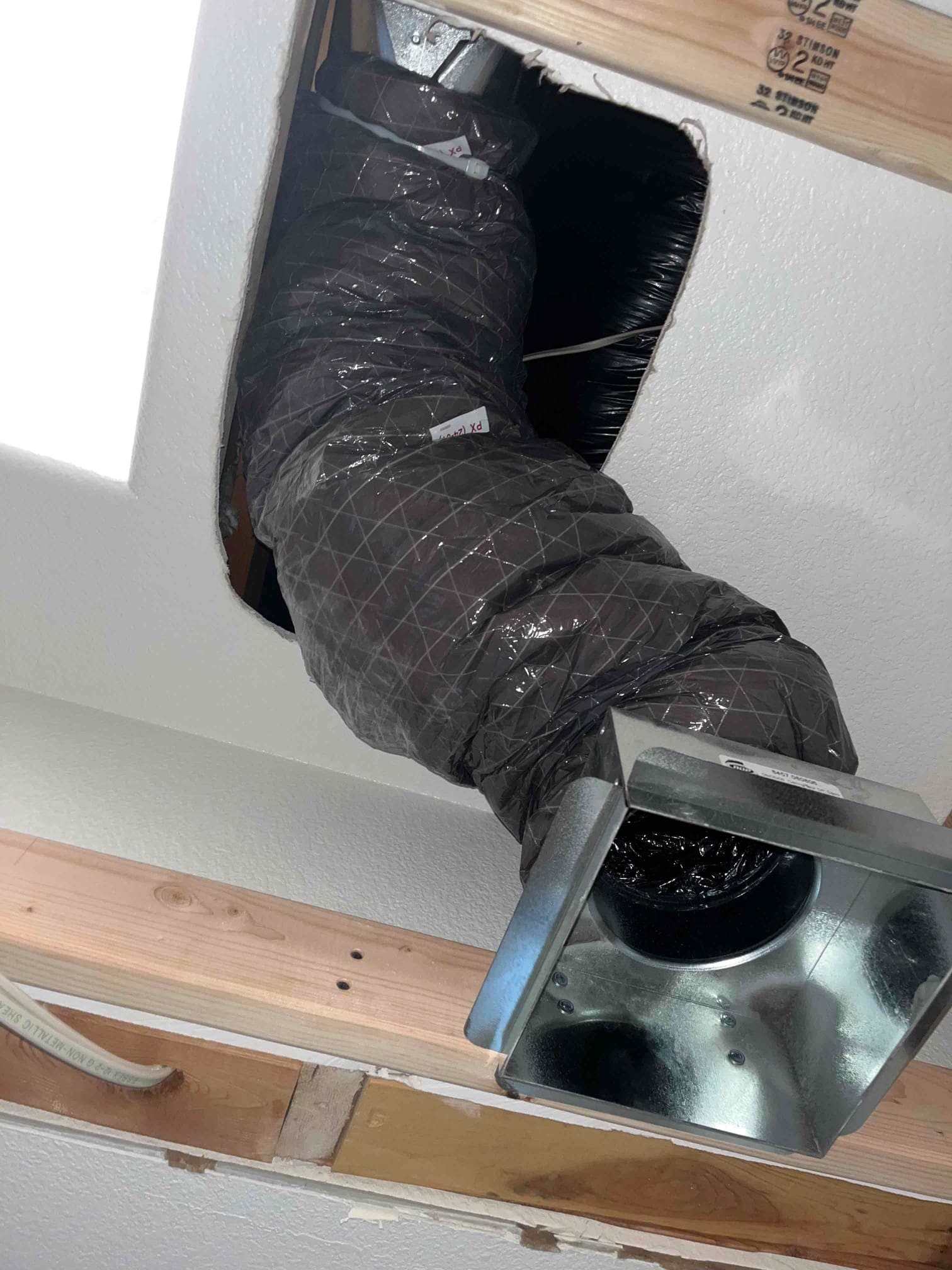 Flexible insulated supply duct routed through ceiling opening with metal boot connected, framing exposed during relocation work.