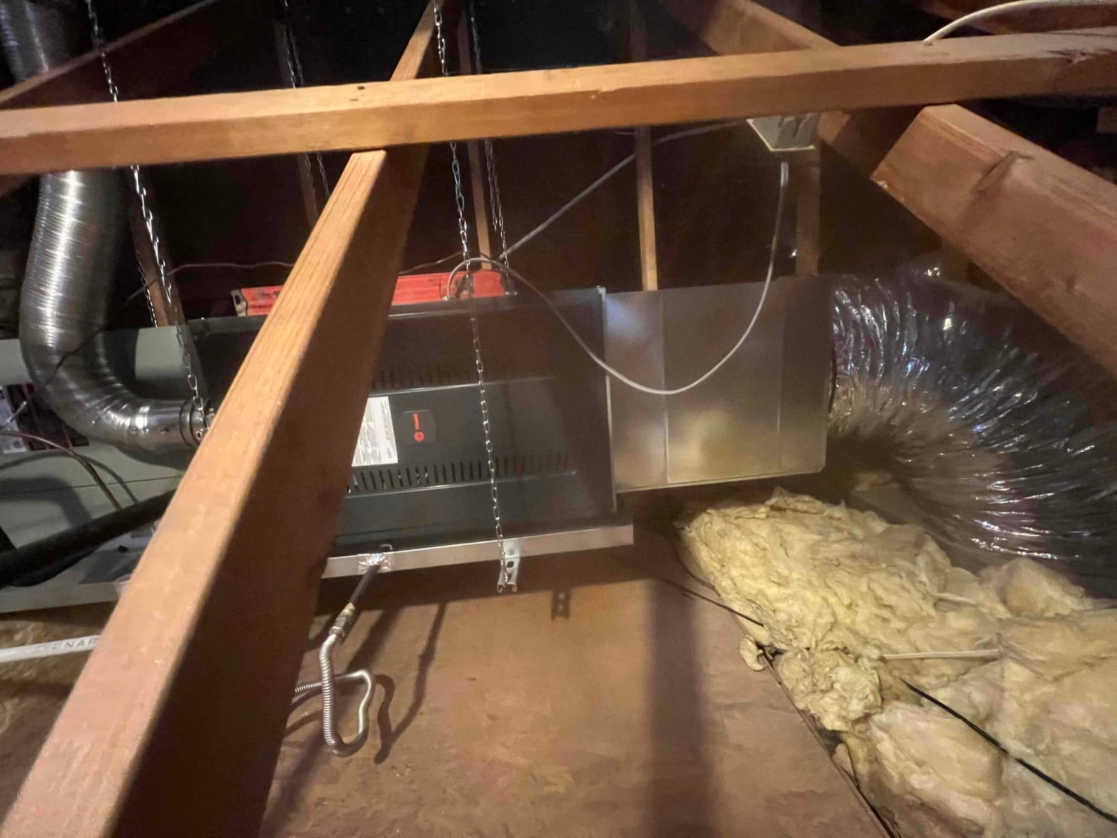 Horizontal air handler suspended in attic with metal transition and insulated flex duct connected, drain and electrical whip visible.