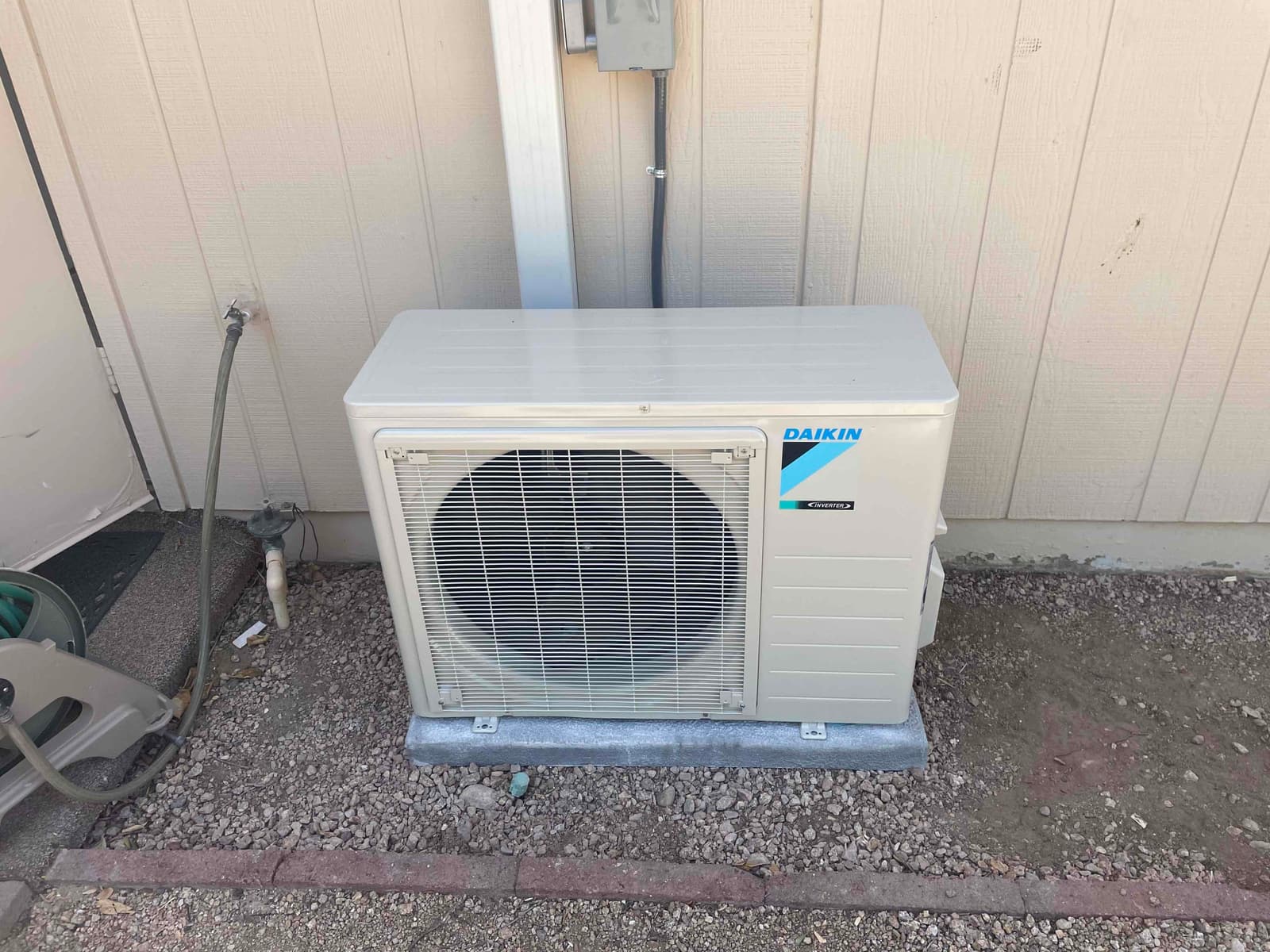 Mini-split outdoor condenser set on a level pad beside the exterior wall with electrical whip and line set cover.