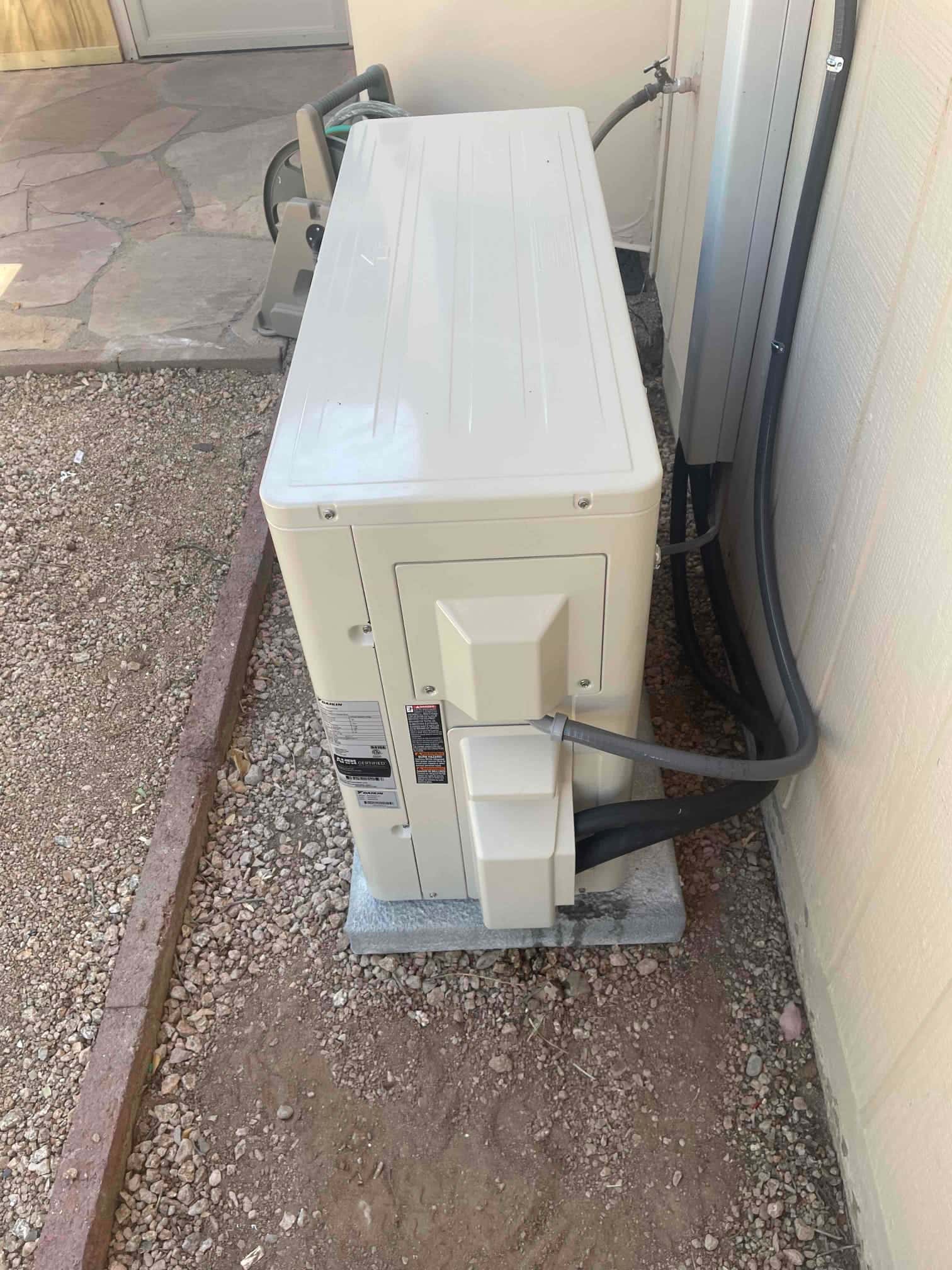 Mini-split outdoor unit set on a level pad with insulated line set and electrical whip routed into the wall.