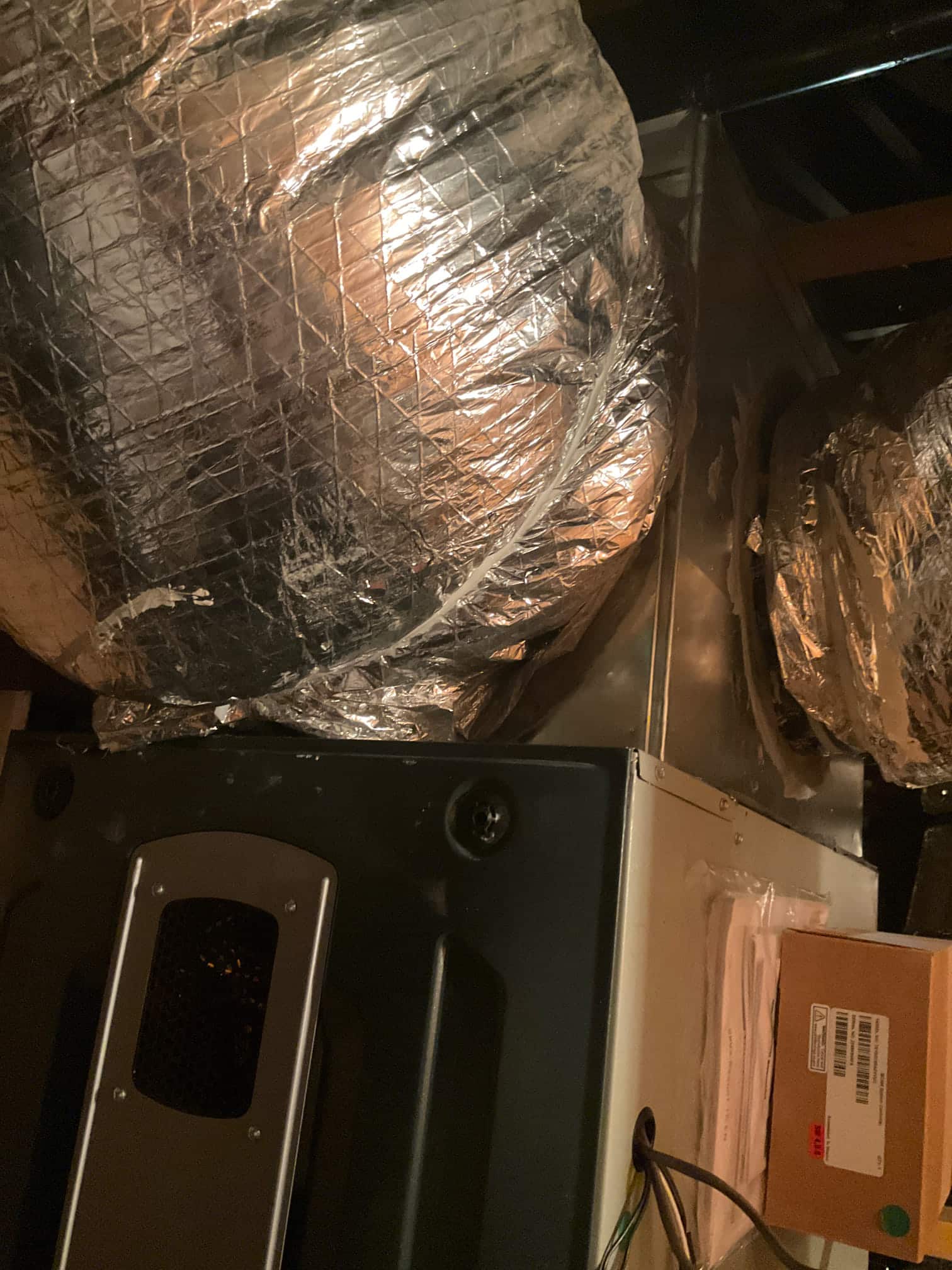 New indoor air handler with insulated flexible duct connections installed and secured, with documentation packet visible on the cabinet side.